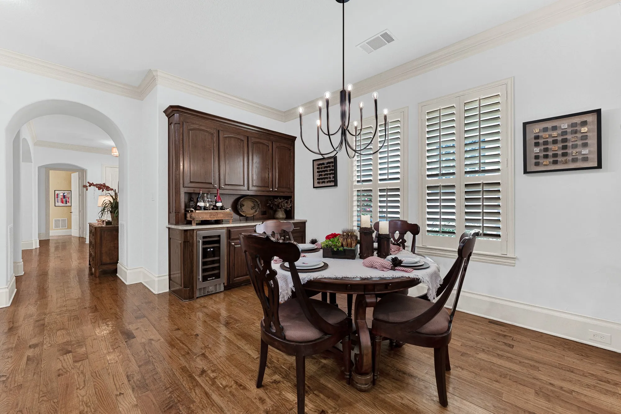 Rich dark wood cabinetry frames a built-in wine cooler beneath custom plantation-shuttered windows. Pour a perfectly chilled glass of Pinot Noir while preparing an intimate dinner for two as night falls.