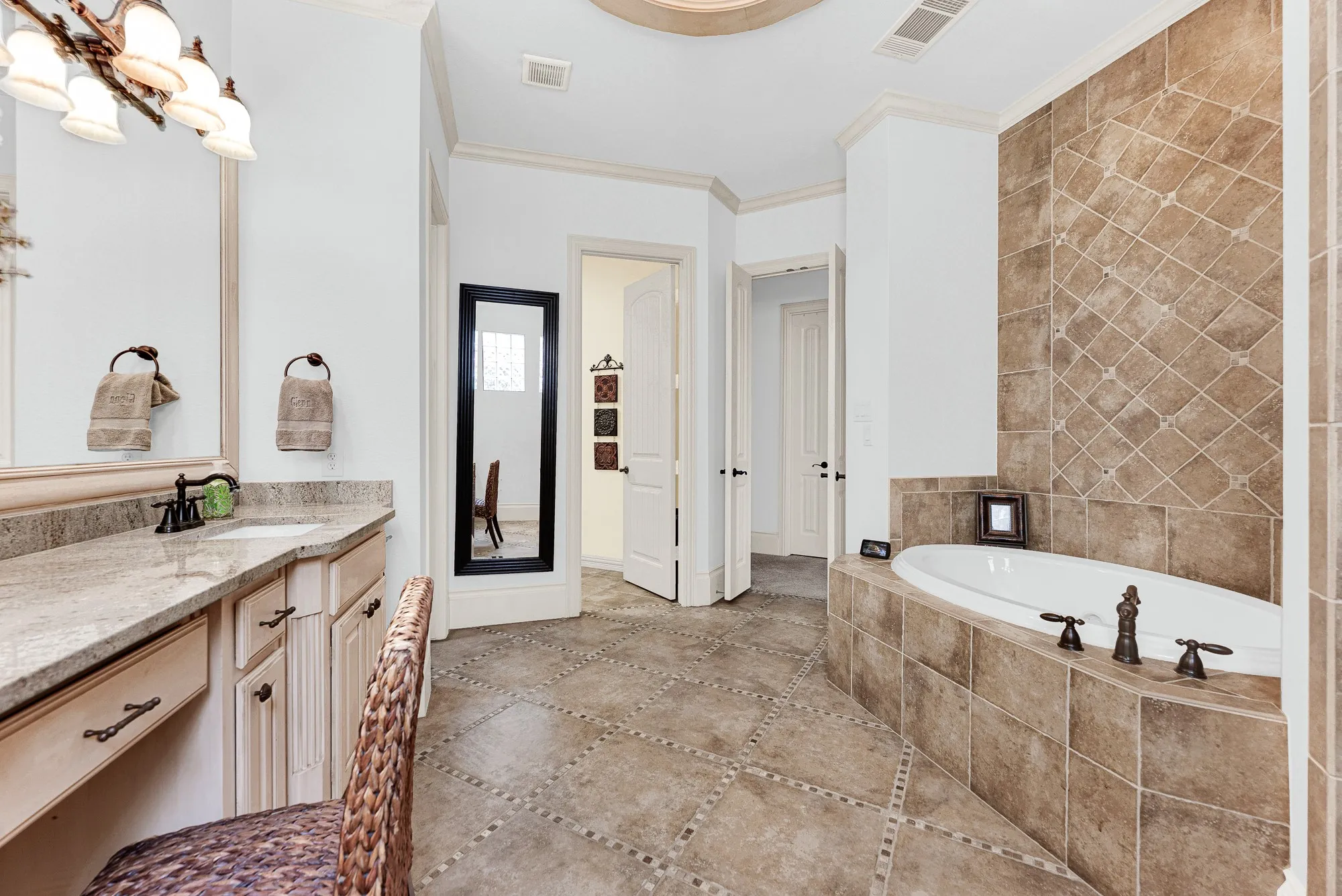 A private doorway connects the en-suite directly to the laundry room for ultimate daily efficiency. Enjoy the effortless convenience of streamlining laundry tasks right steps from your closet. Earth-toned tile extends floor-to-ceiling behind the deep jetted soaking tub, adding rich texture to the quiet corner. Indulge in an extended evening soak surrounded by calm, neutral finishes.