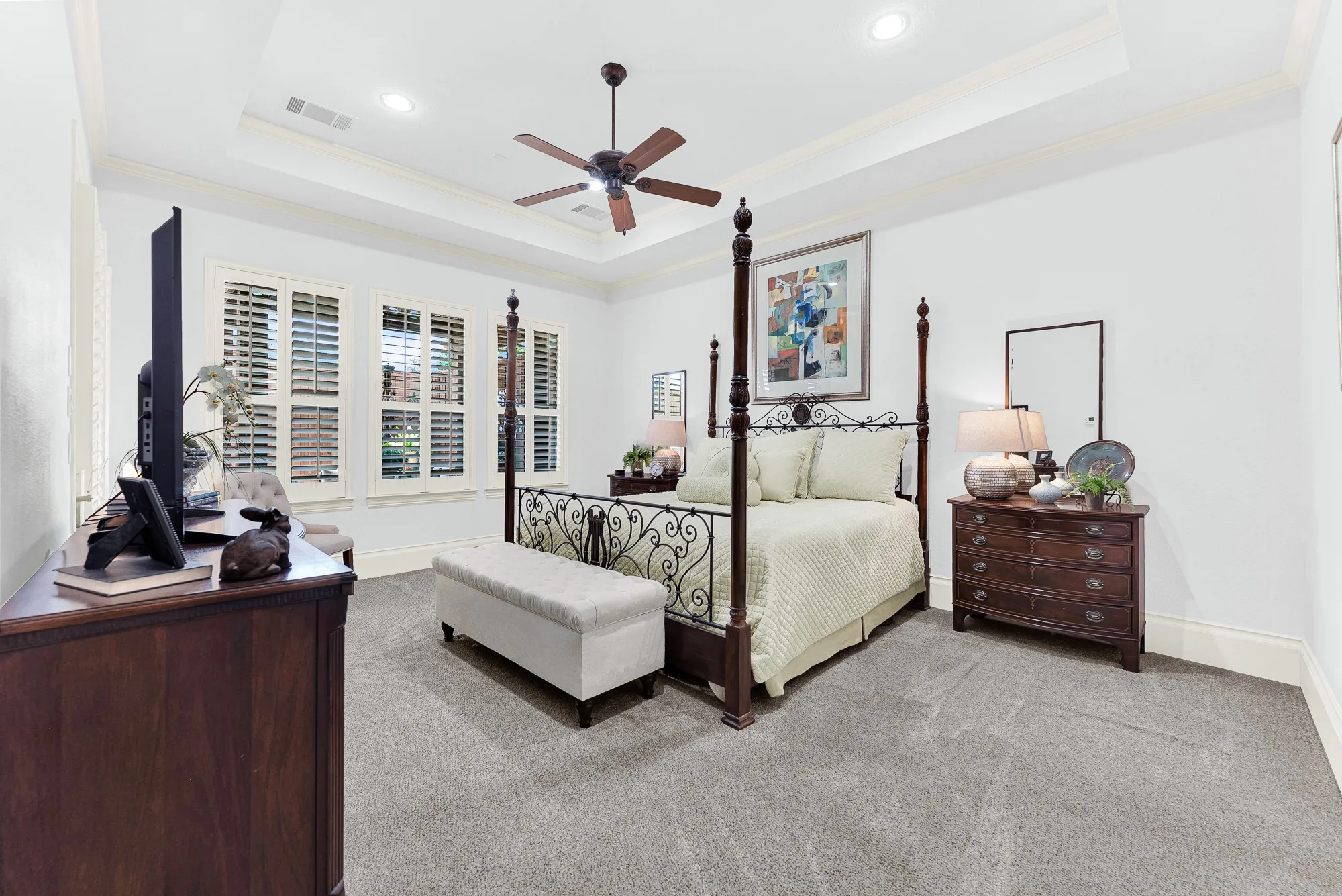 A multi-tiered tray ceiling lifts the eye, while wide window shutters softly temper incoming daylight across plush carpeting. Drift off effortlessly at night in this peaceful, private sleeping quarters