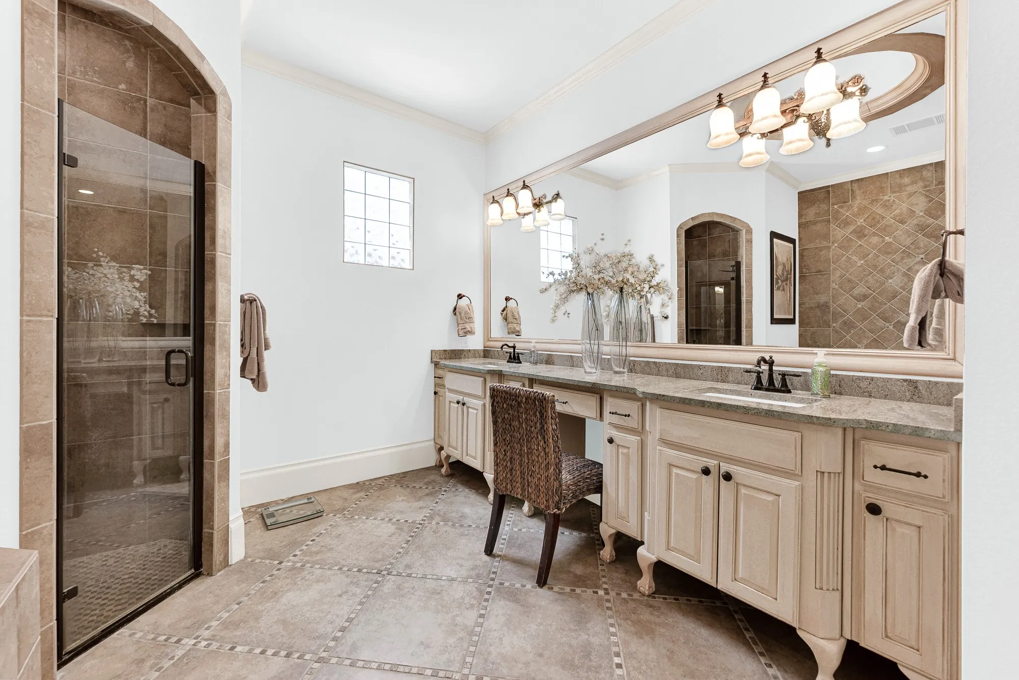 An expansive double vanity with a seated makeup station stretches beneath a wall-mounted glass mirror. Complete your morning skincare routine with plenty of room to stretch out and organize.