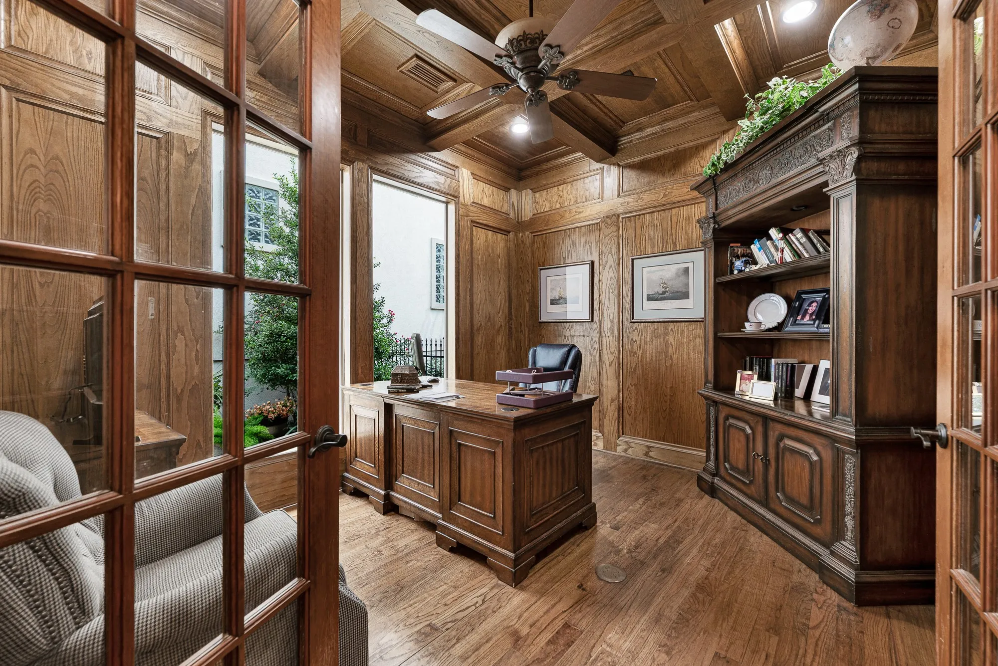 Rich wood wainscoting and a detailed coffered ceiling frame natural daylight streaming through full-height courtyard windows. Settle in for focused morning work while enjoying calming views of lush outdoor greenery