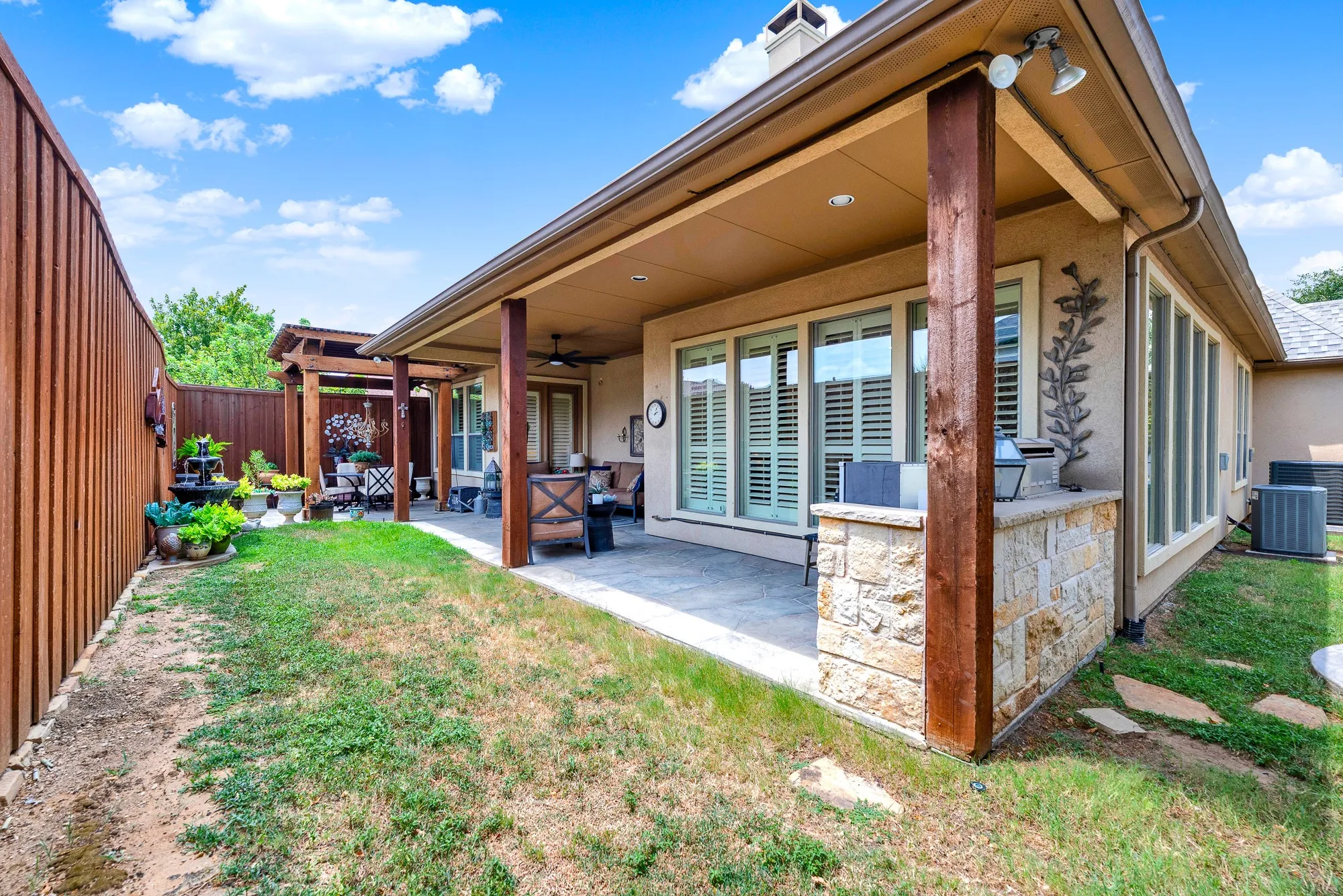 A built-in stone grill station anchors the shaded veranda beneath a high porch ceiling. Visualize serving fresh appetizers to guests as afternoon shadows stretch gracefully across the yard. Expansive window banks flood the home with sunshine while connecting to a circular stone patio pad. Enjoy a quiet weekend afternoon listening to the breeze rustle through mature shade trees.
