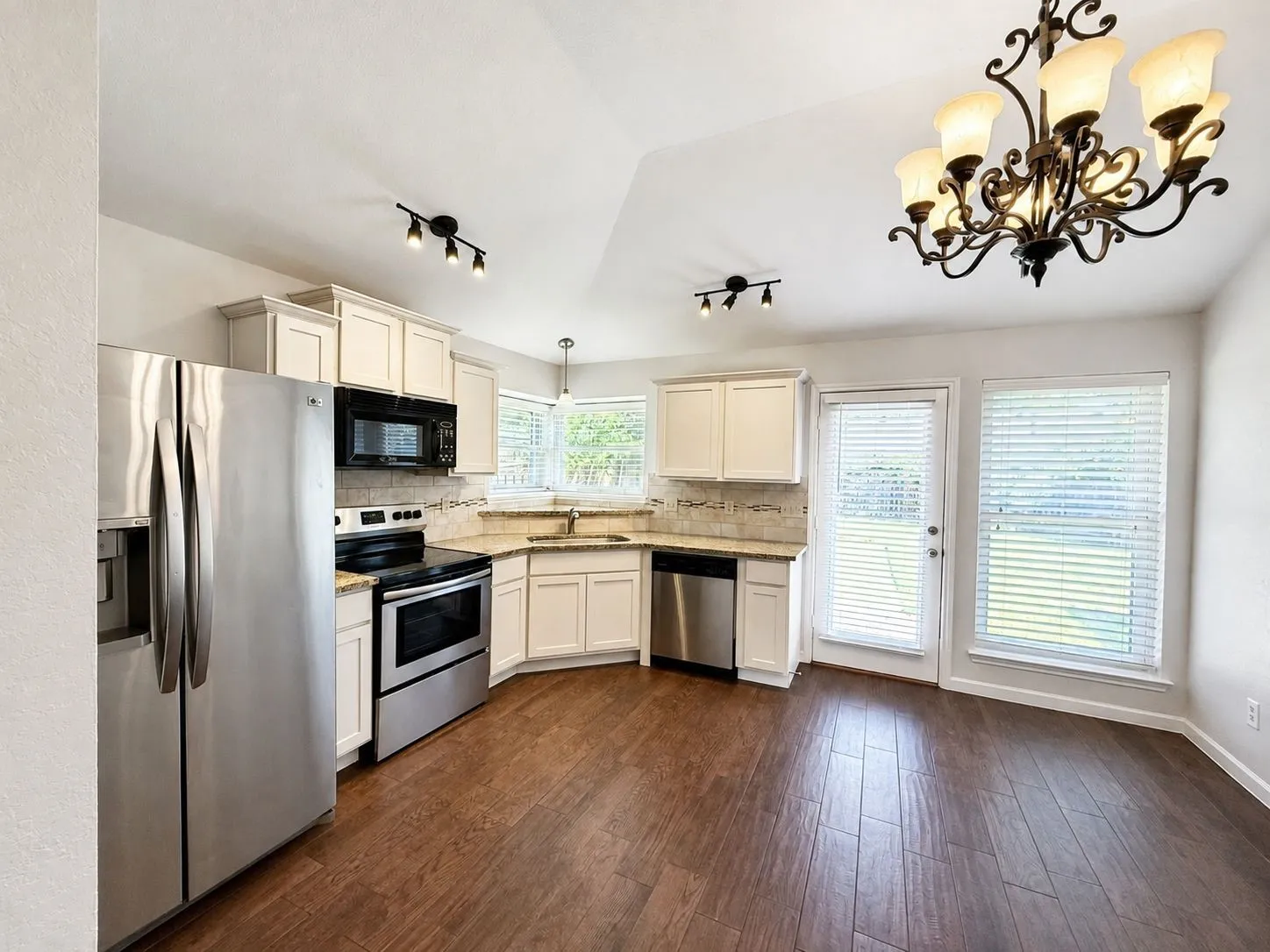 Vaulted ceiling, wood-finish flooring, white cabinetry, integrated stainless steel appliances, and a decorative chandelier