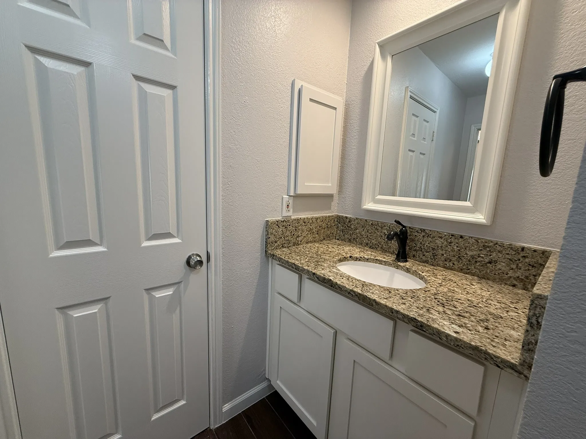 White vanity with shaker-style cabinetry, granite countertop, oval undermount sink, and oil-rubbed bronze faucet