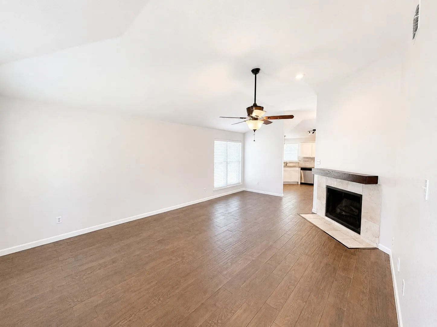 Vaulted ceilings, wood-finish flooring, ceiling fan, fireplace with stone surround, and a wood mantel