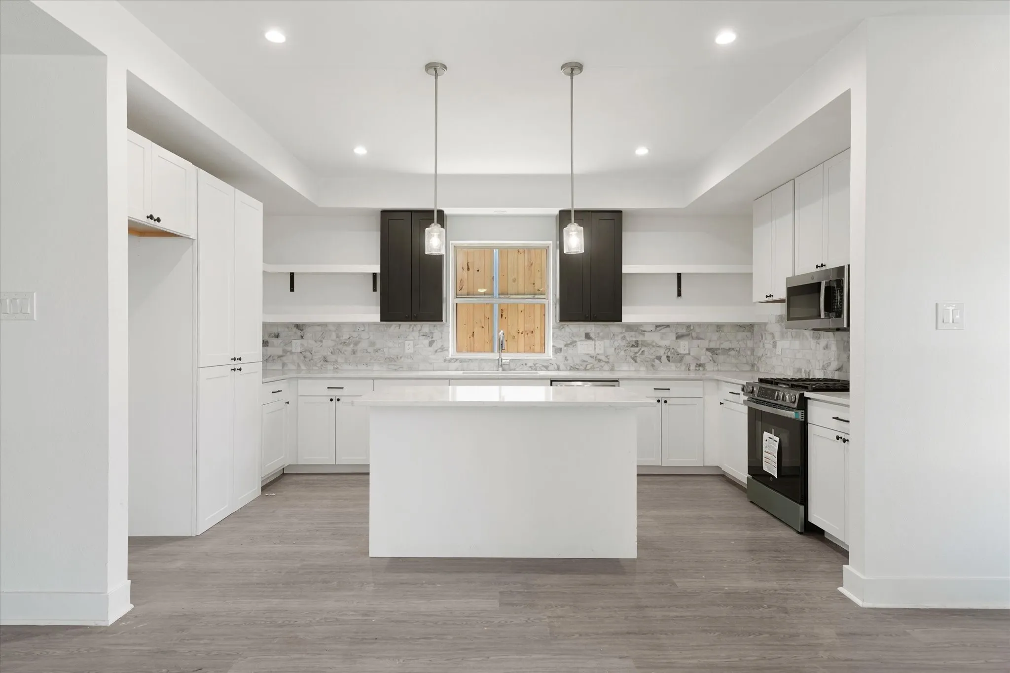 Modern kitchen with a central island, white cabinetry, integrated stainless-steel appliances, marble-look backsplash, and wood-finish flooring