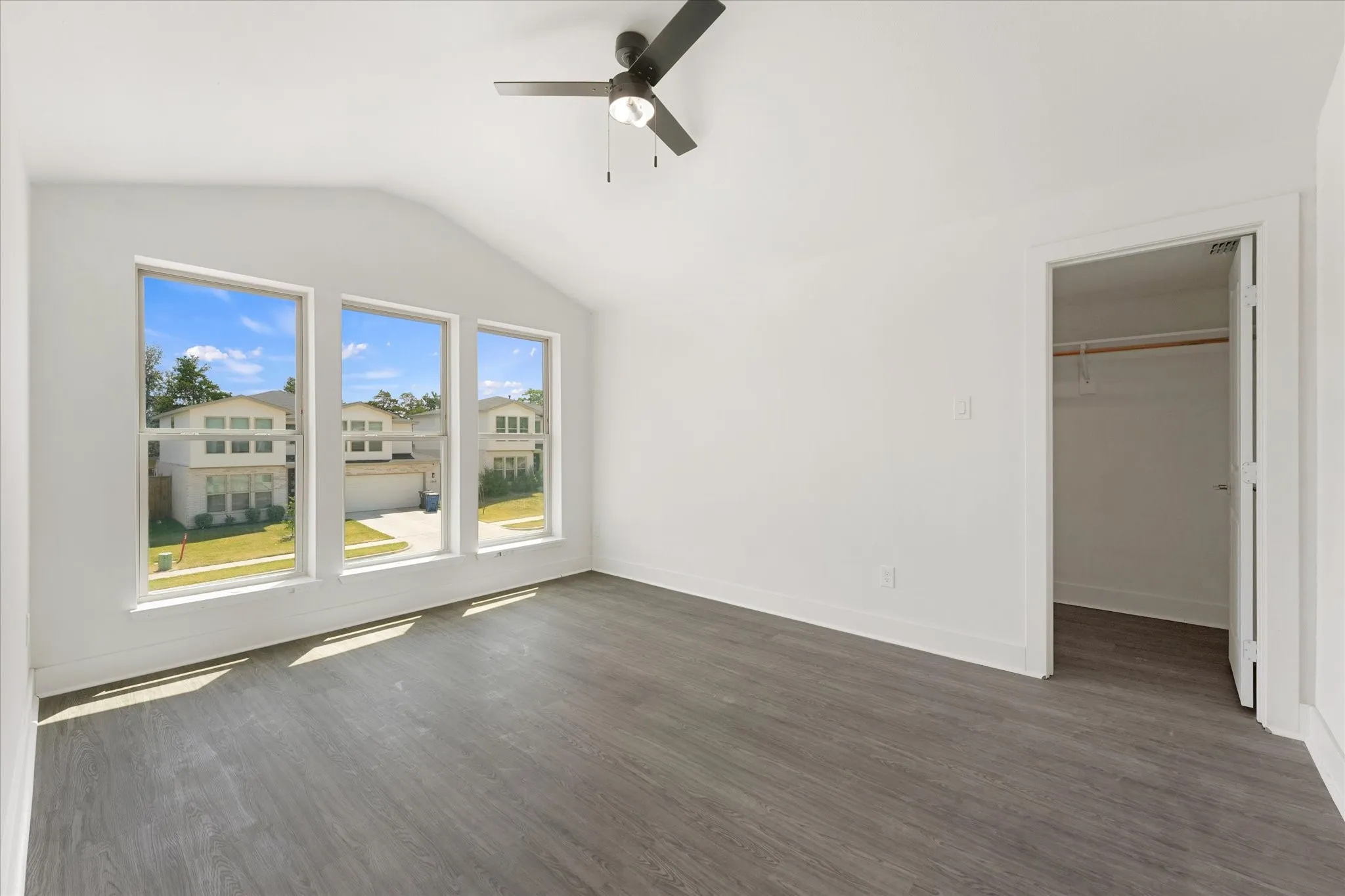 Vaulted ceiling, three large windows, wood-finish flooring, ceiling fan, and a built-in closet with hanging rod