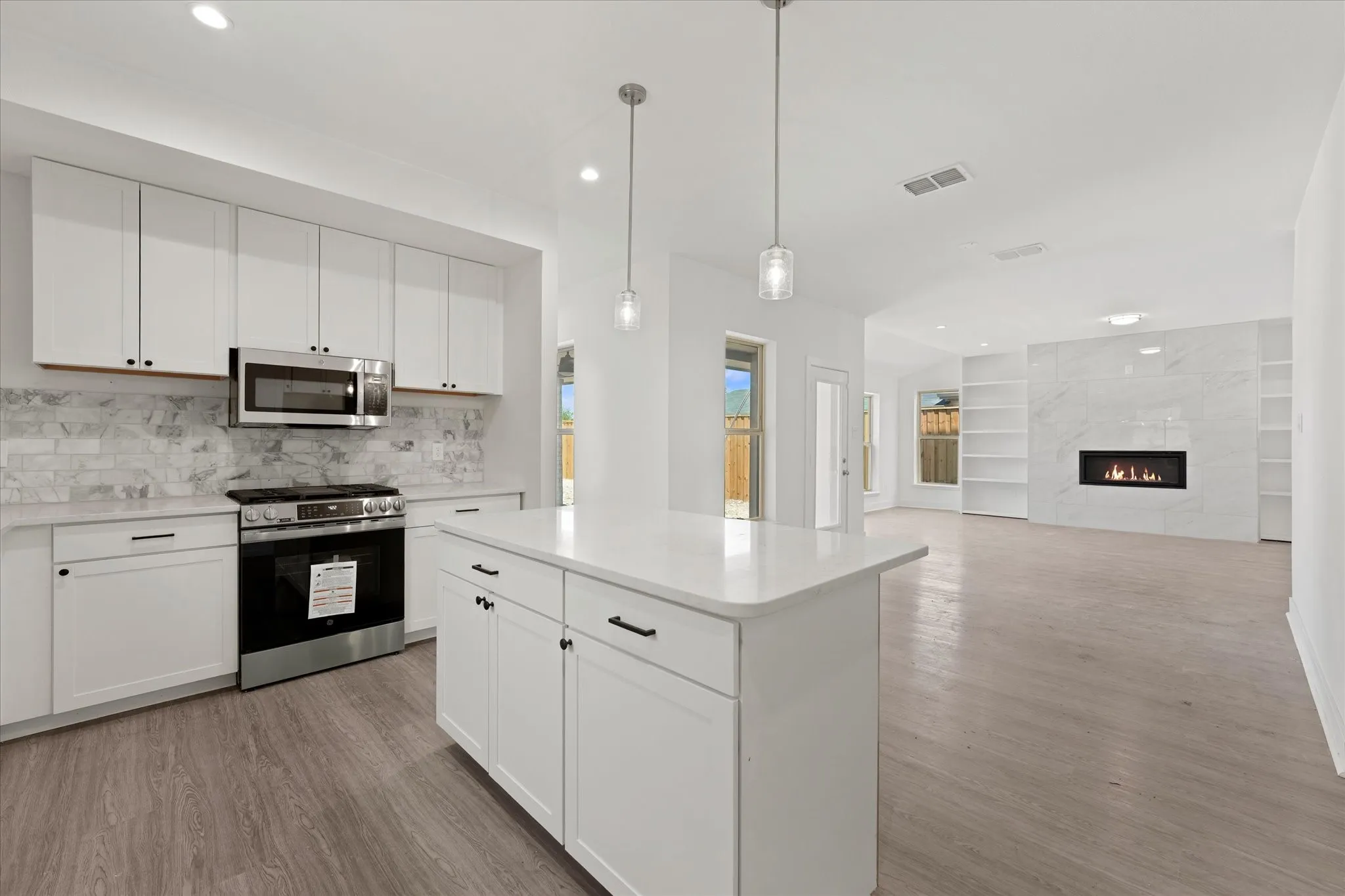 Kitchen island with white countertops, white cabinetry with black hardware, stainless steel range and microwave, and wood-finish flooring