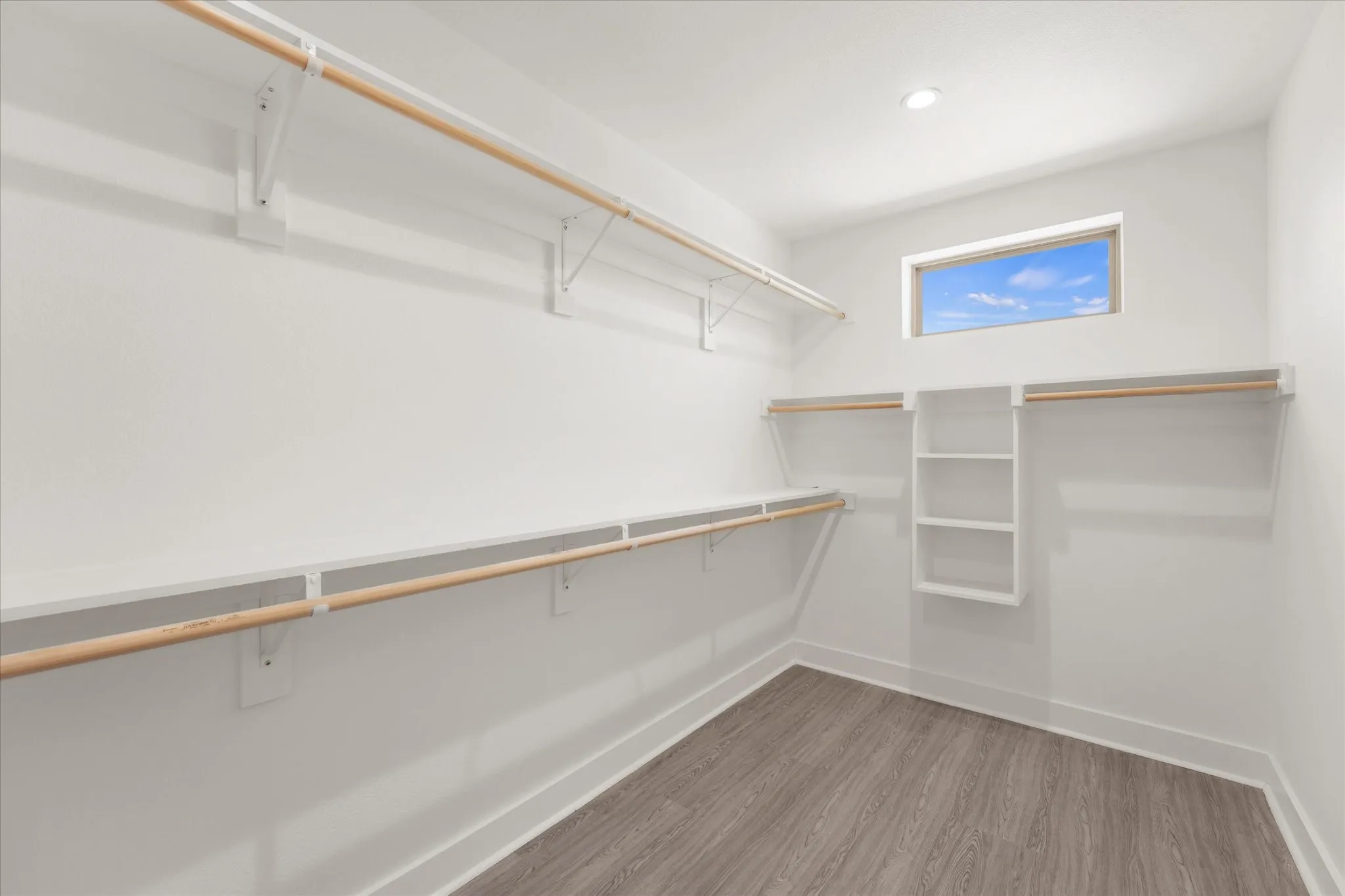 Recessed lighting, wood-finish flooring, white walls, built-in shelving, and a horizontal window