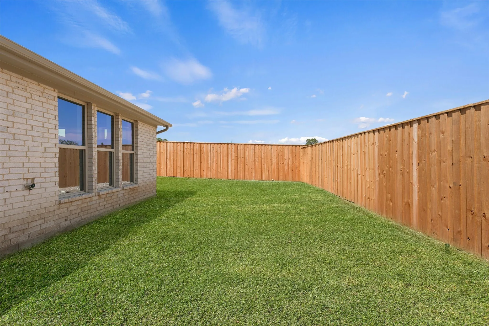 Expansive backyard featuring a manicured lawn, a full wood privacy fence, and a brick exterior with multiple windows