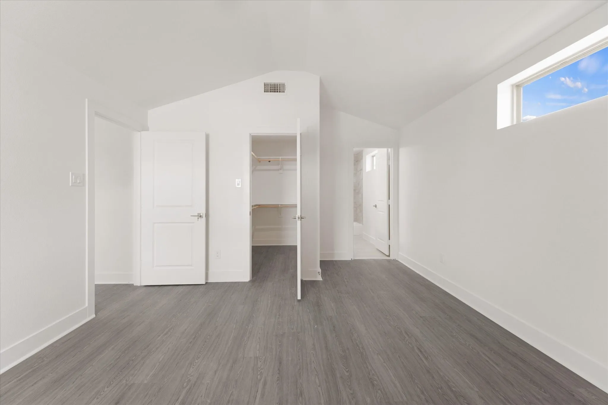 Vaulted ceiling, high horizontal window, wood-finish flooring, two-panel interior doors, and a built-in closet with shelving