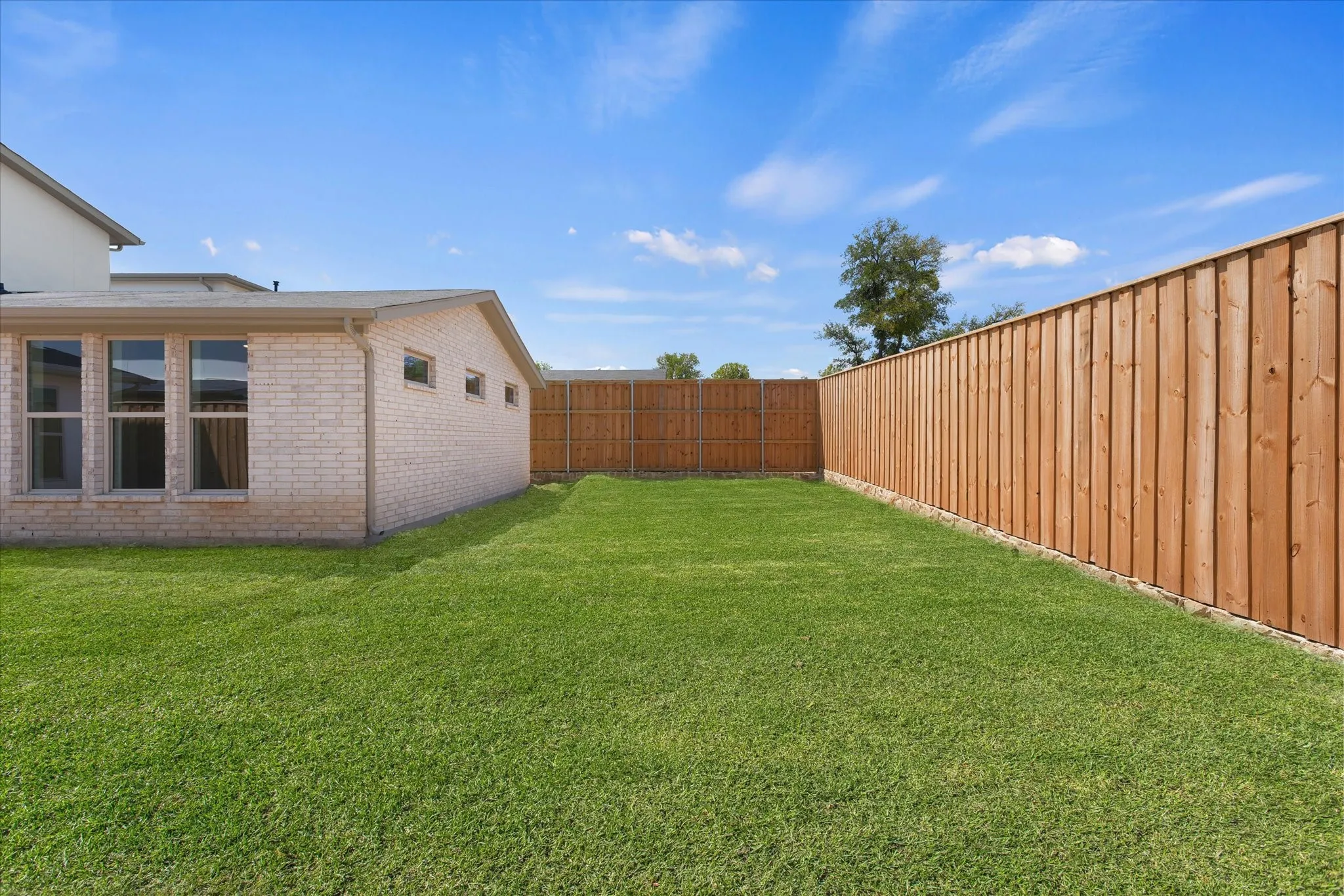 Expansive backyard featuring a manicured lawn, full privacy fencing, and a brick exterior