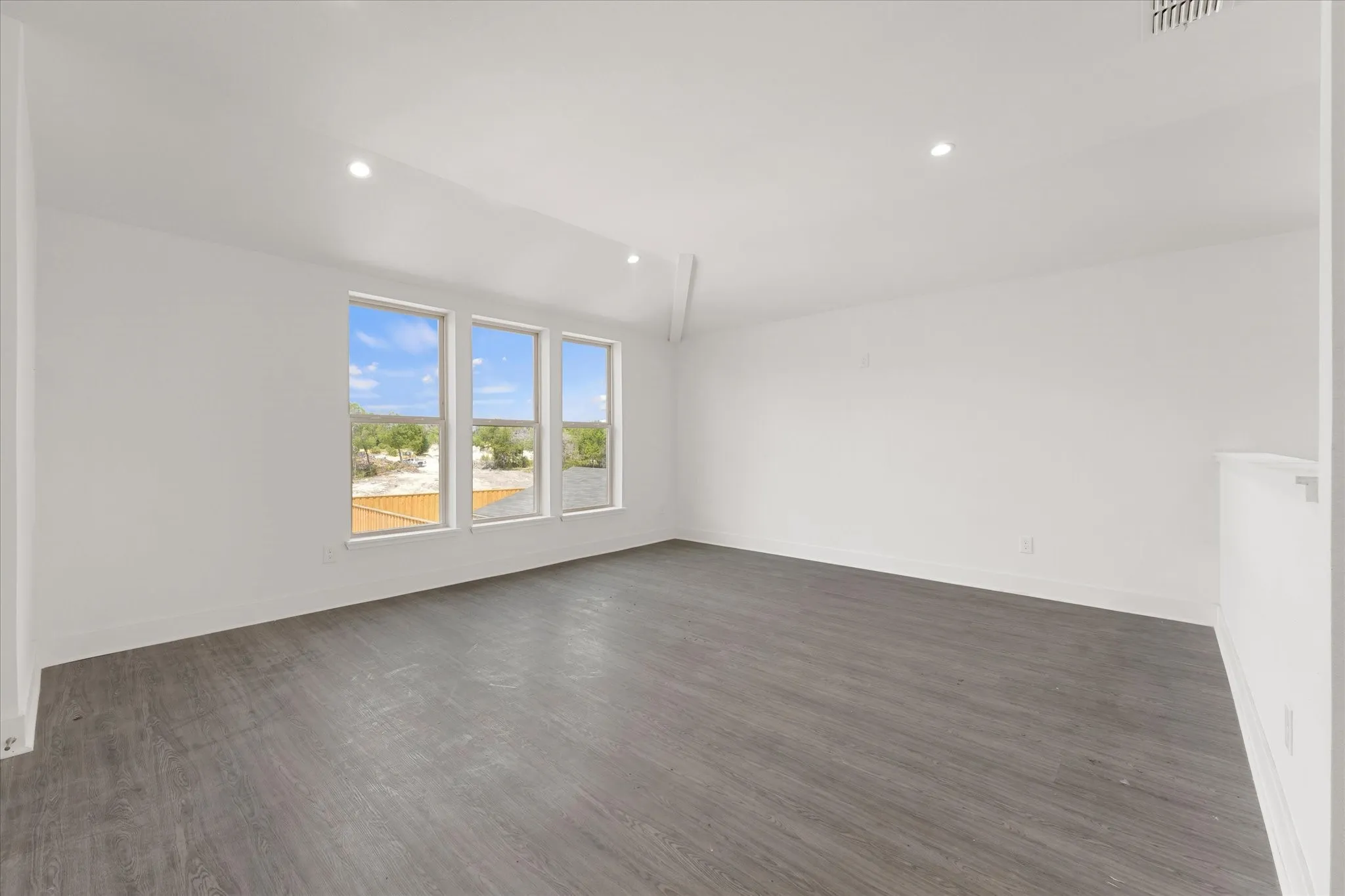 Spacious room featuring wood-finish flooring, recessed lighting, and three tall windows