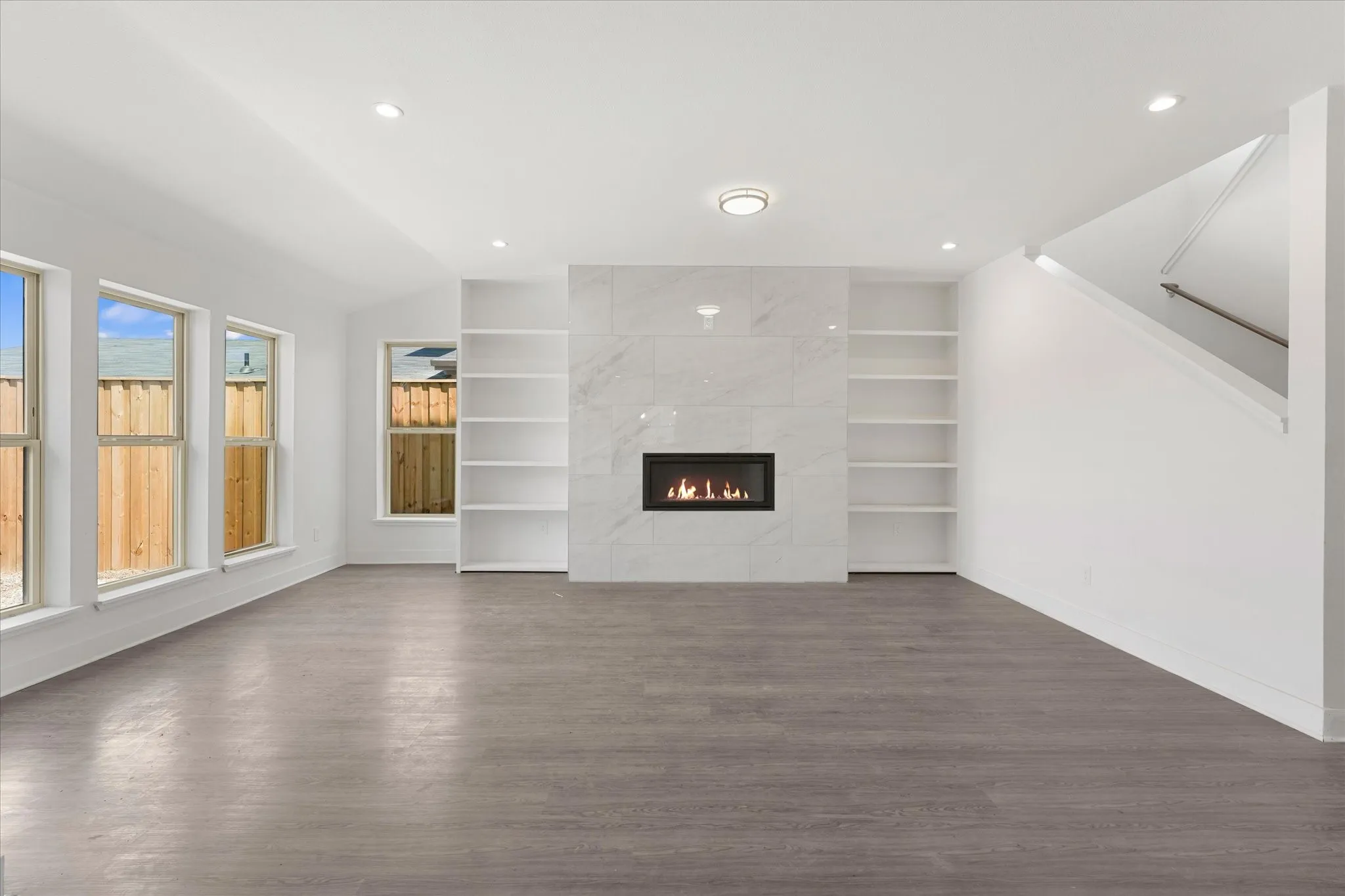 Expansive living area featuring wood-finish flooring, a contemporary fireplace with a stone-finish surround, built-in shelving, and recessed lighting