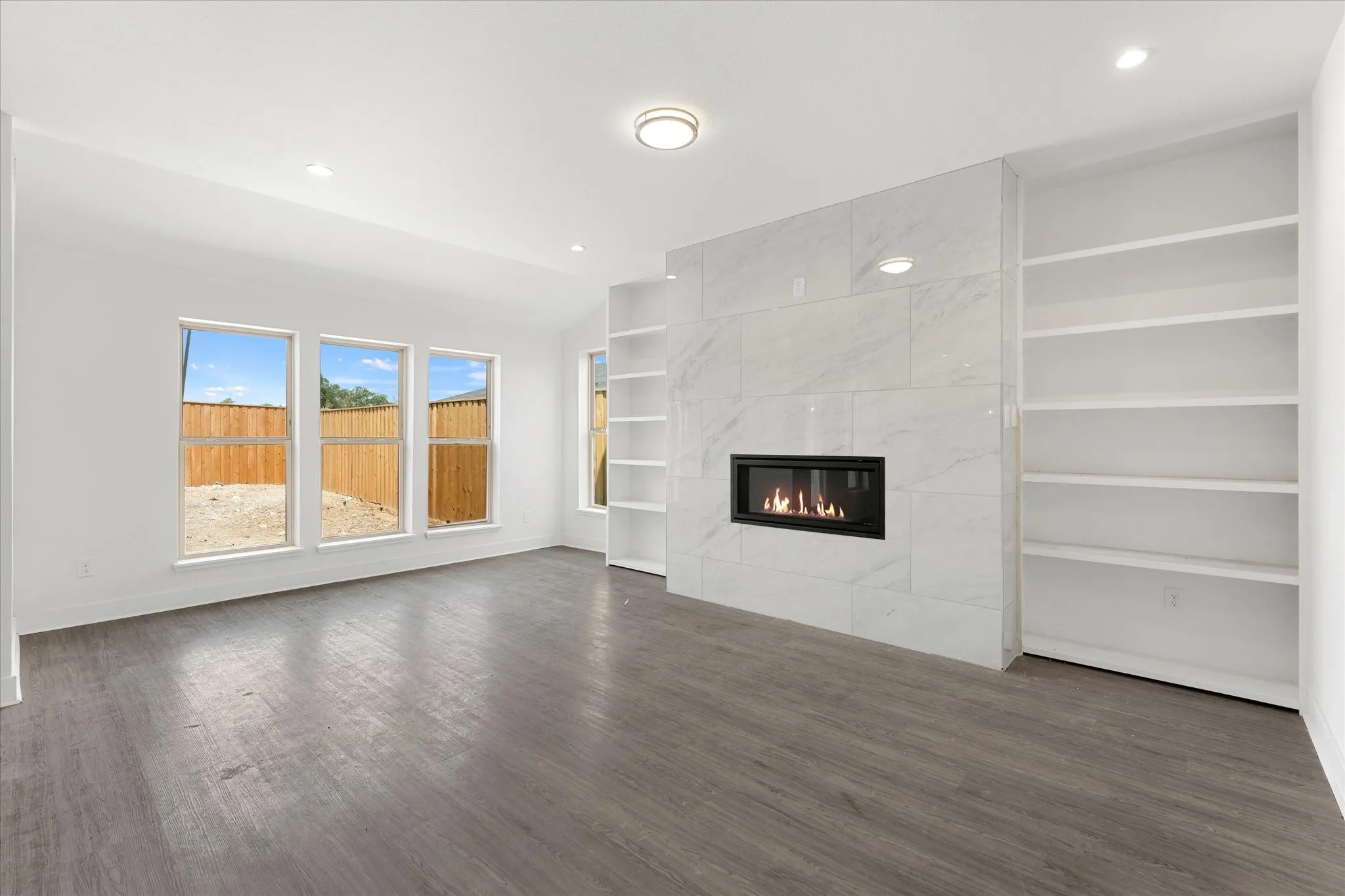 Wood-finish flooring, recessed lighting, and a linear fireplace set within a tile surround