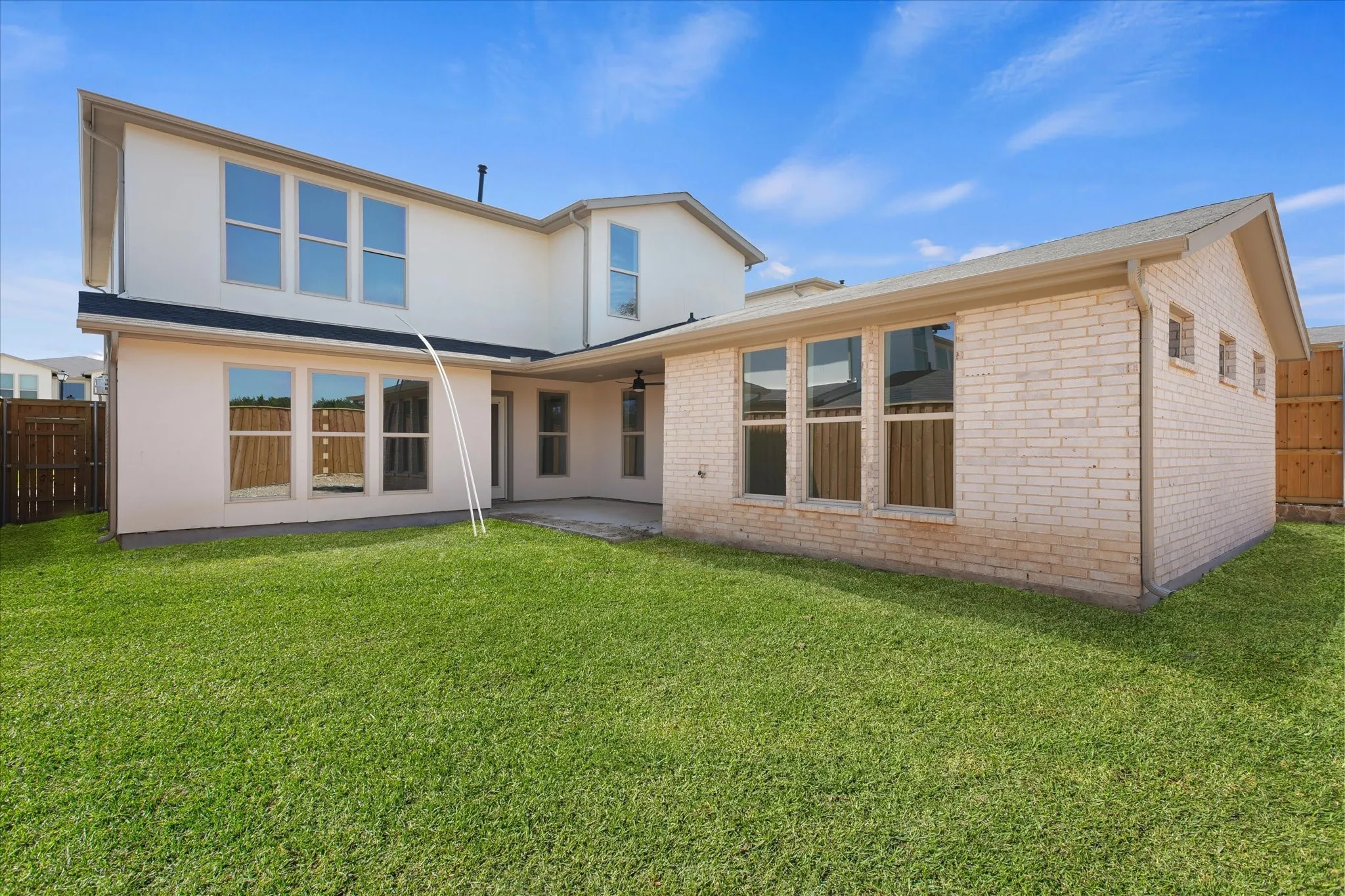 Expansive green lawn with a covered patio, featuring a two-story stucco exterior and a single-story brick wing