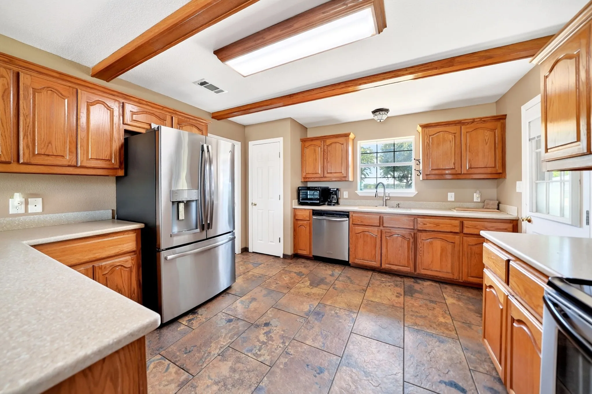 Kitchen featuring wood cabinetry, stone-look tile flooring, and exposed wood beams