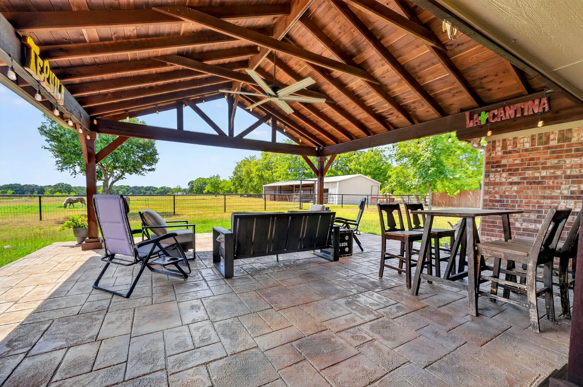 Expansive covered patio featuring a wood-beam ceiling, ceiling fan, stamped concrete flooring, and a brick exterior wall