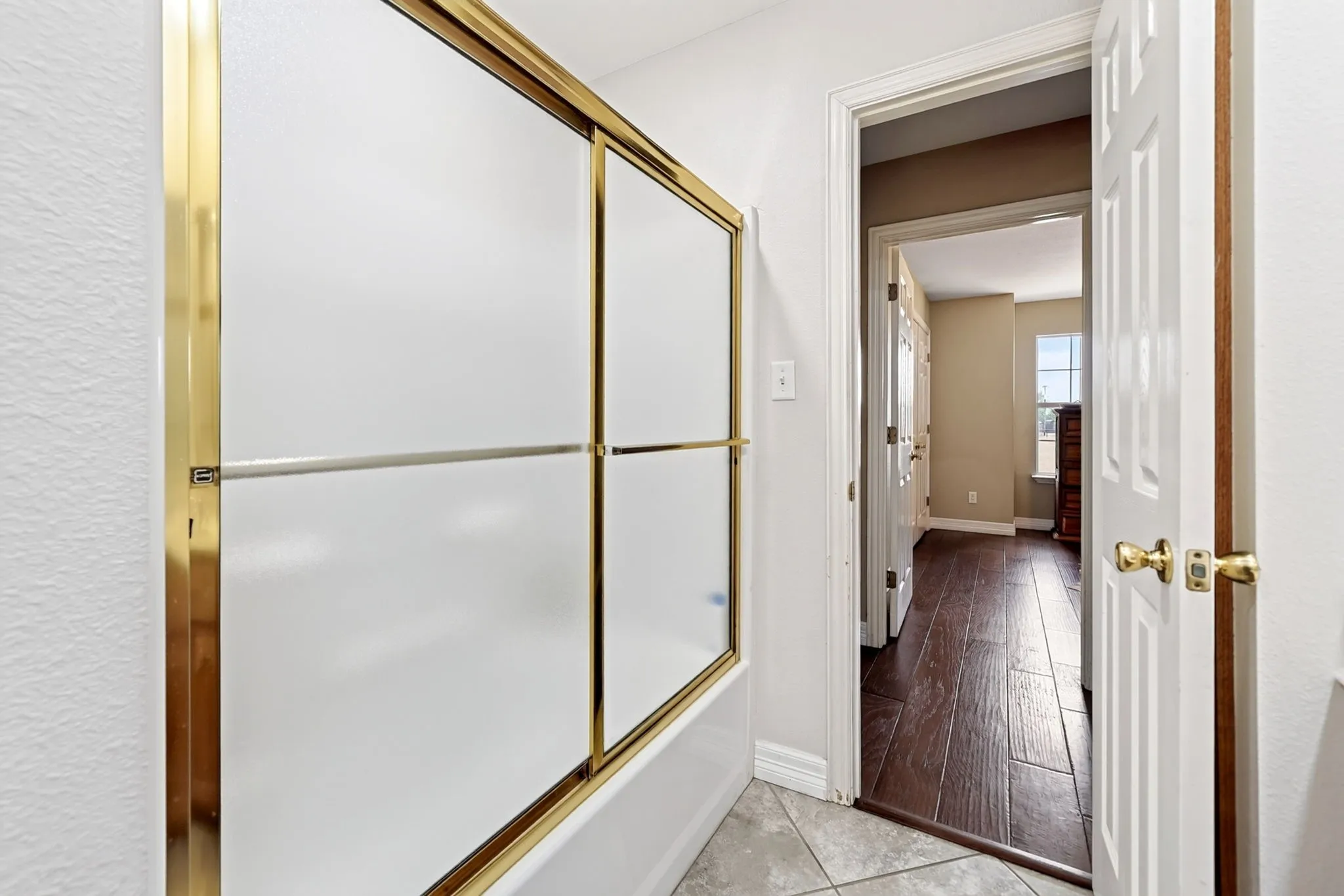 Bathtub with gold-finish sliding shower doors, white paneled door, and gold-finish hardware