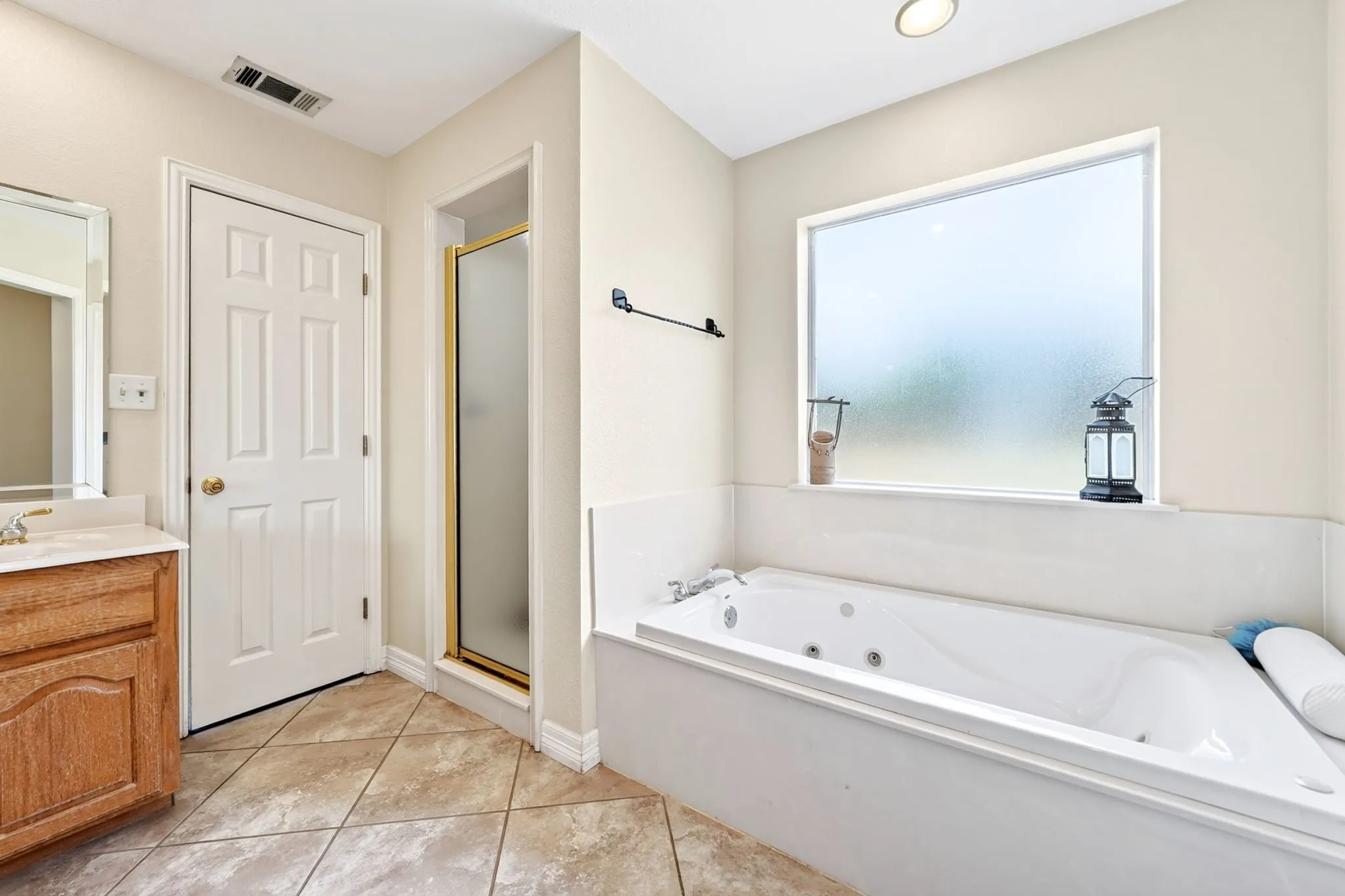 Tiled flooring, built-in soaking tub, frosted window, gold-framed shower, and wood vanity with integrated sink