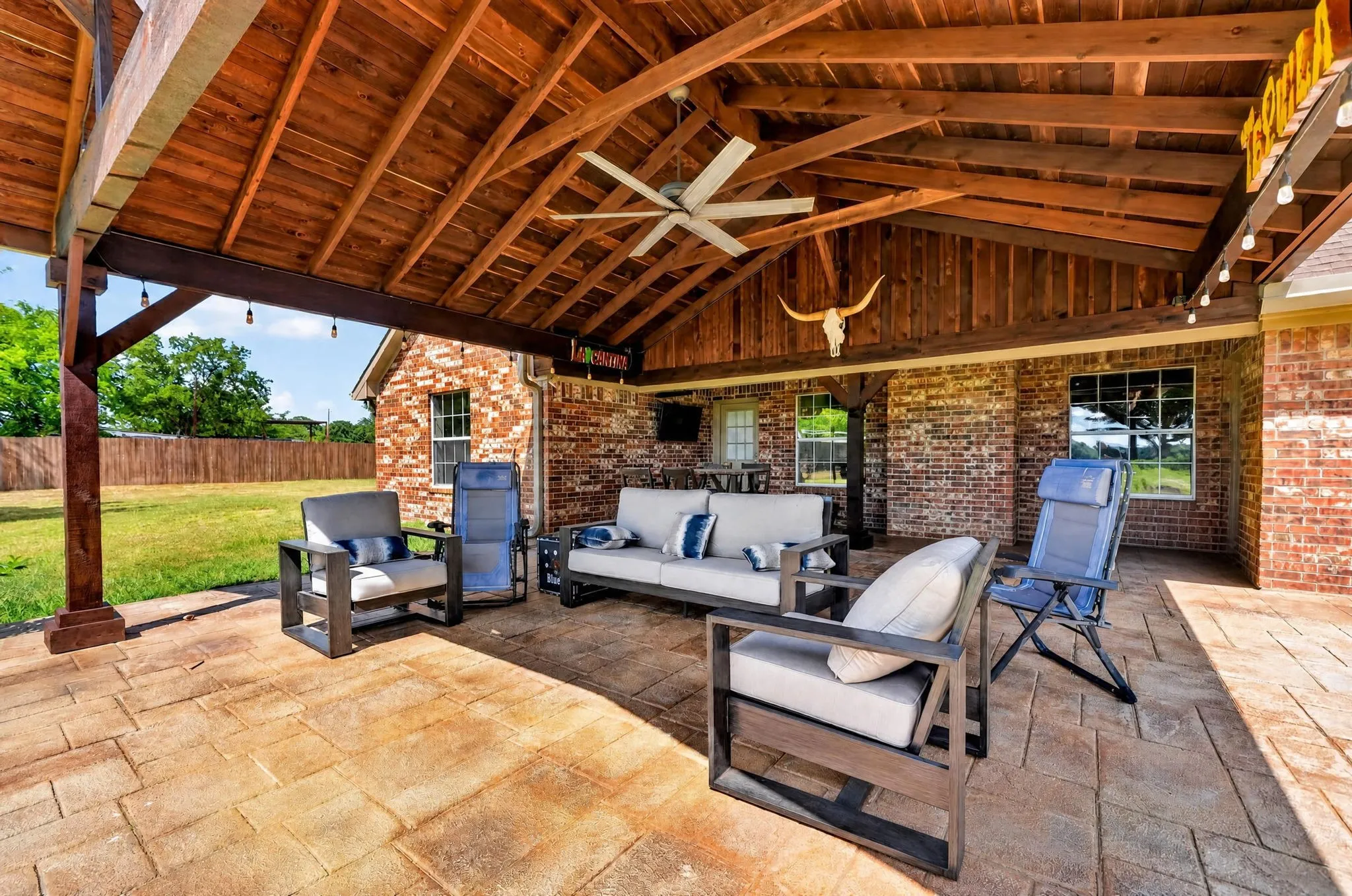 Expansive covered patio featuring a vaulted wood-plank ceiling, exposed wood beams, and a ceiling fan