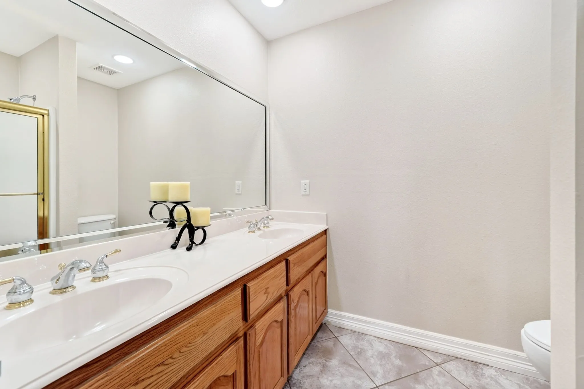 Dual vanity with integrated sinks, wood-finish cabinetry, a full-width mirror, and tile flooring