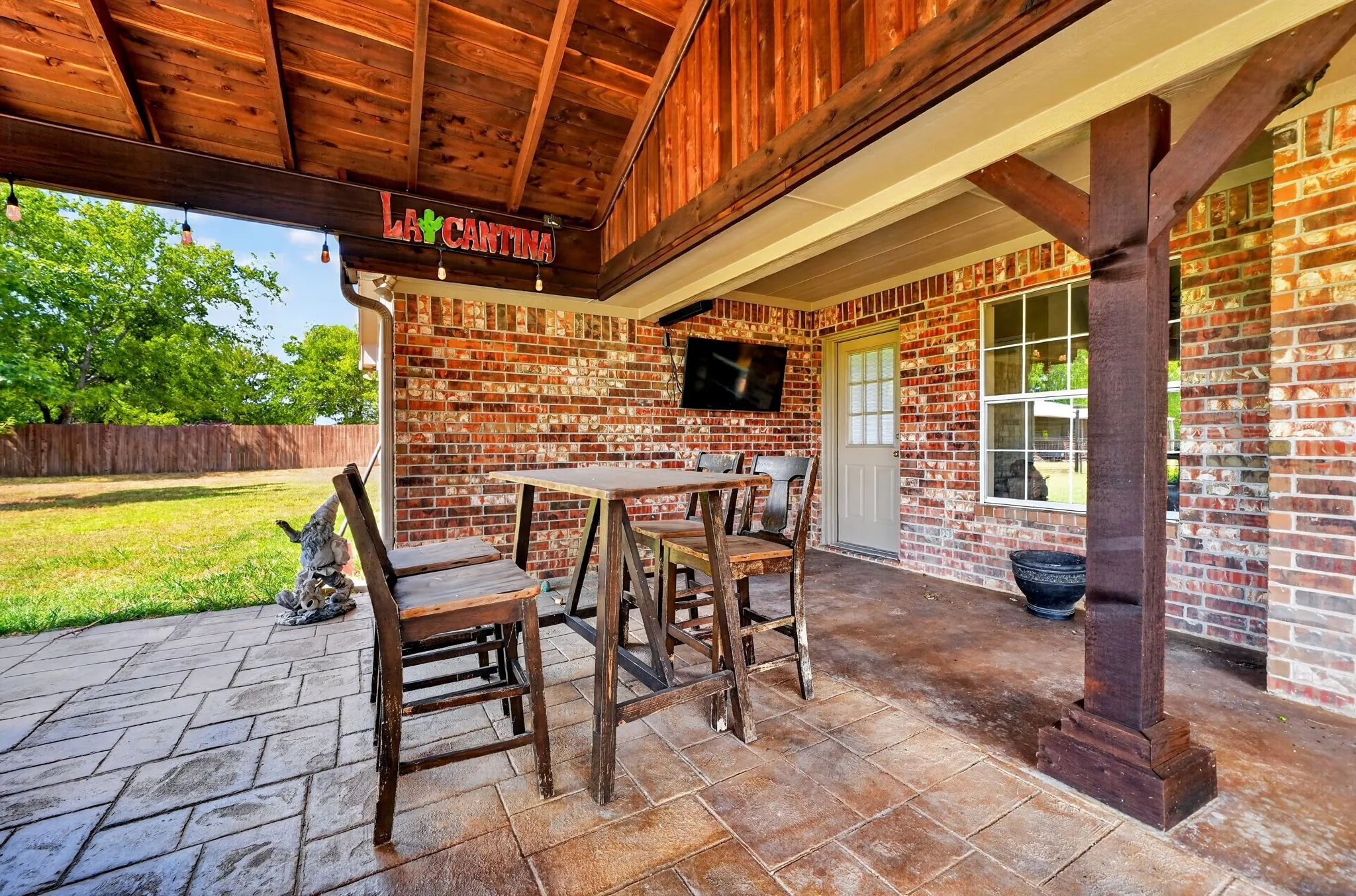 Covered patio featuring a wood-plank ceiling, brick exterior, stamped concrete flooring, and a large window
