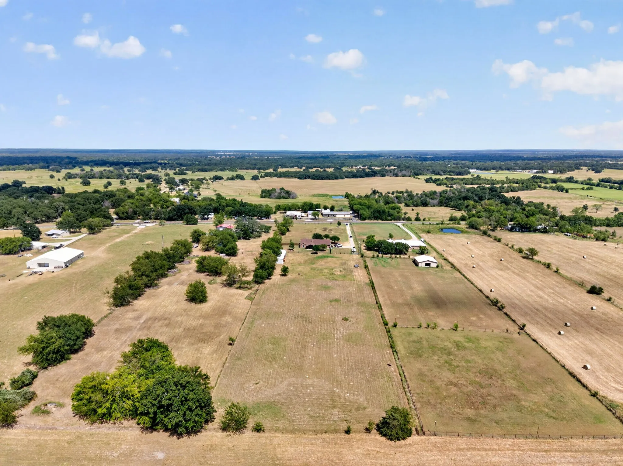 Expansive rural landscape with multiple outbuildings, fenced parcels, scattered mature trees, and a pond feature
