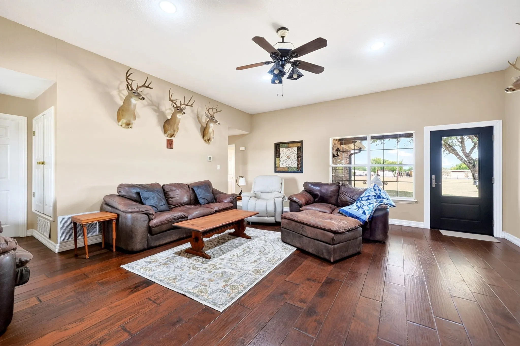 Wood-finish flooring, a ceiling fan with integrated lighting, a large window with exterior visibility, and a glass-paneled entry door