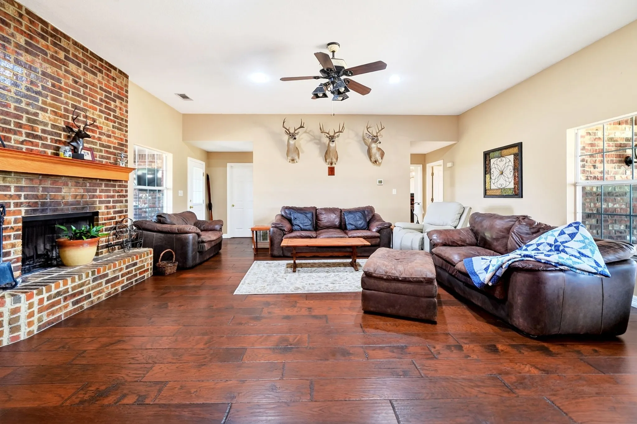 Spacious living area featuring a brick fireplace with a wood mantel, wood-finish flooring, and a ceiling fan