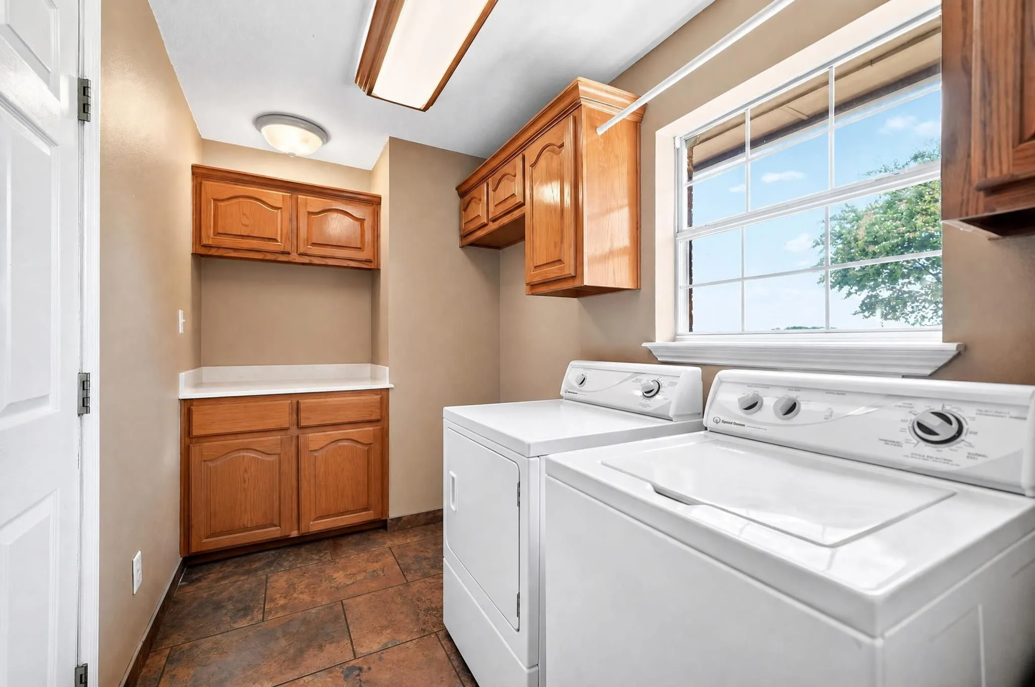 Integrated laundry area with tile flooring, wood cabinetry, built-in countertop space, and overhead lighting