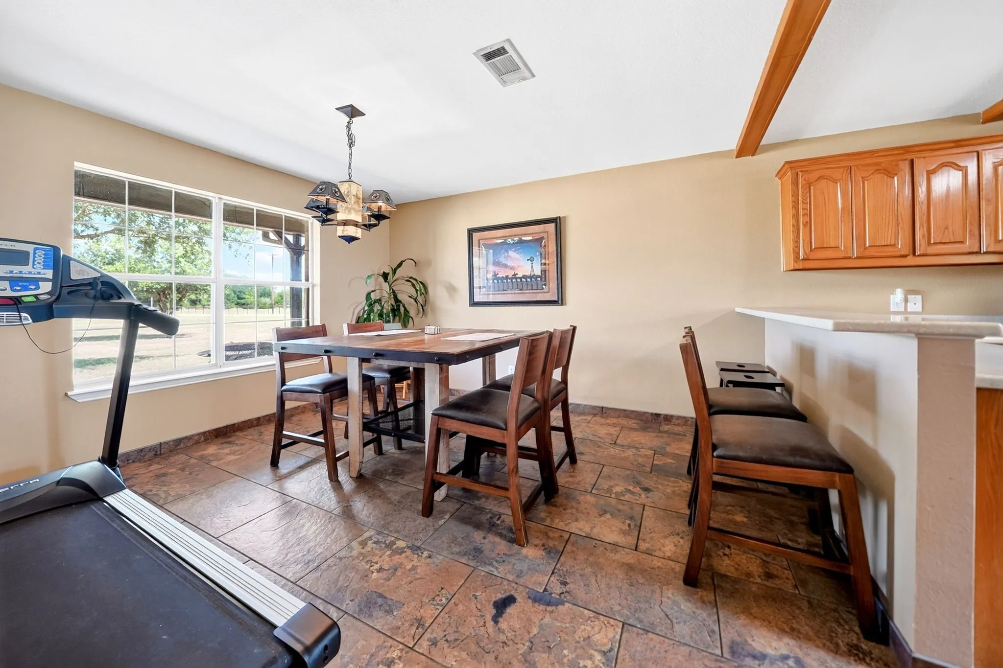 Rectangular window, tiled flooring, built-in breakfast bar, upper wood cabinetry, and a decorative ceiling light fixture