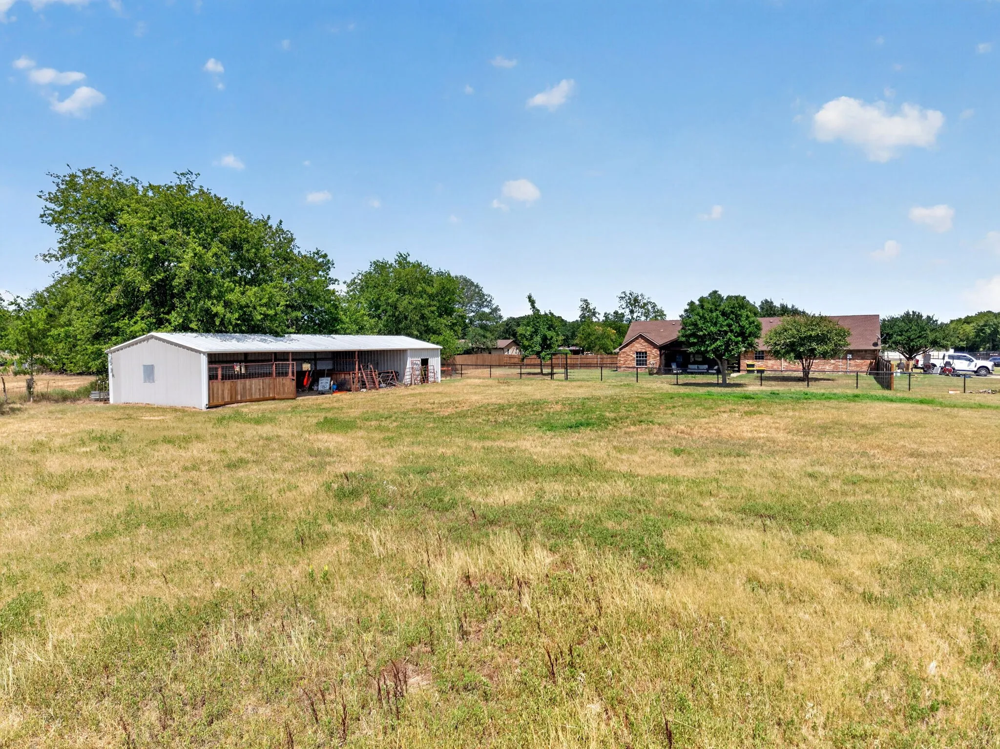Expansive grassy area with a detached metal building and a brick-clad structure