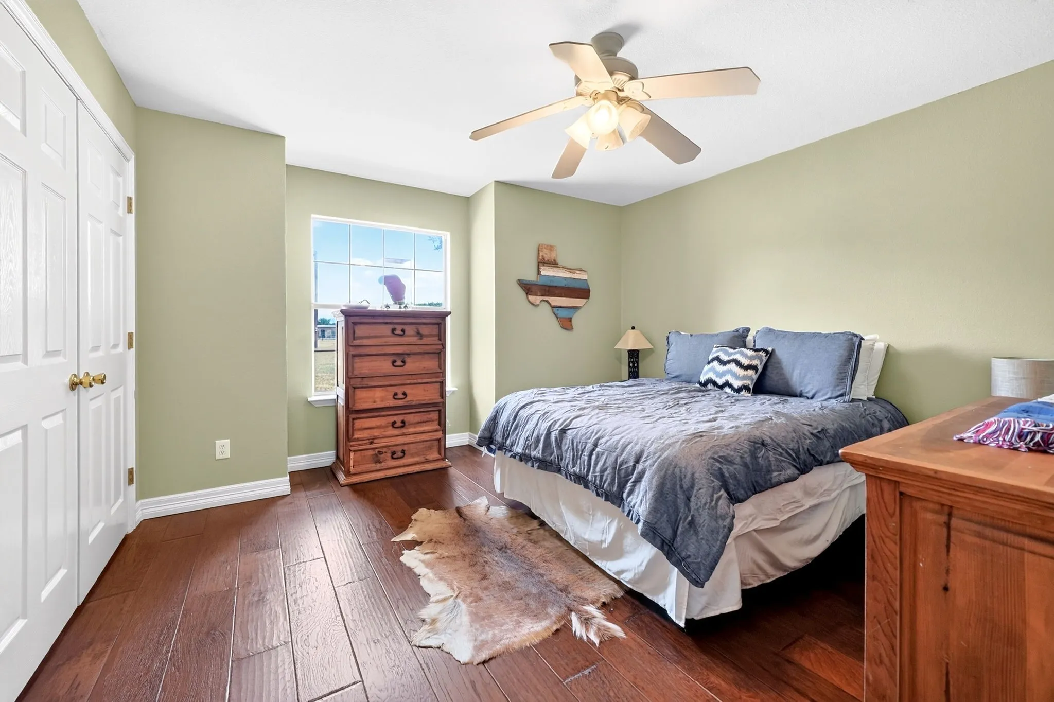 Wood-finish flooring, ceiling fan with integrated lighting, double-door closet, and window with a white frame