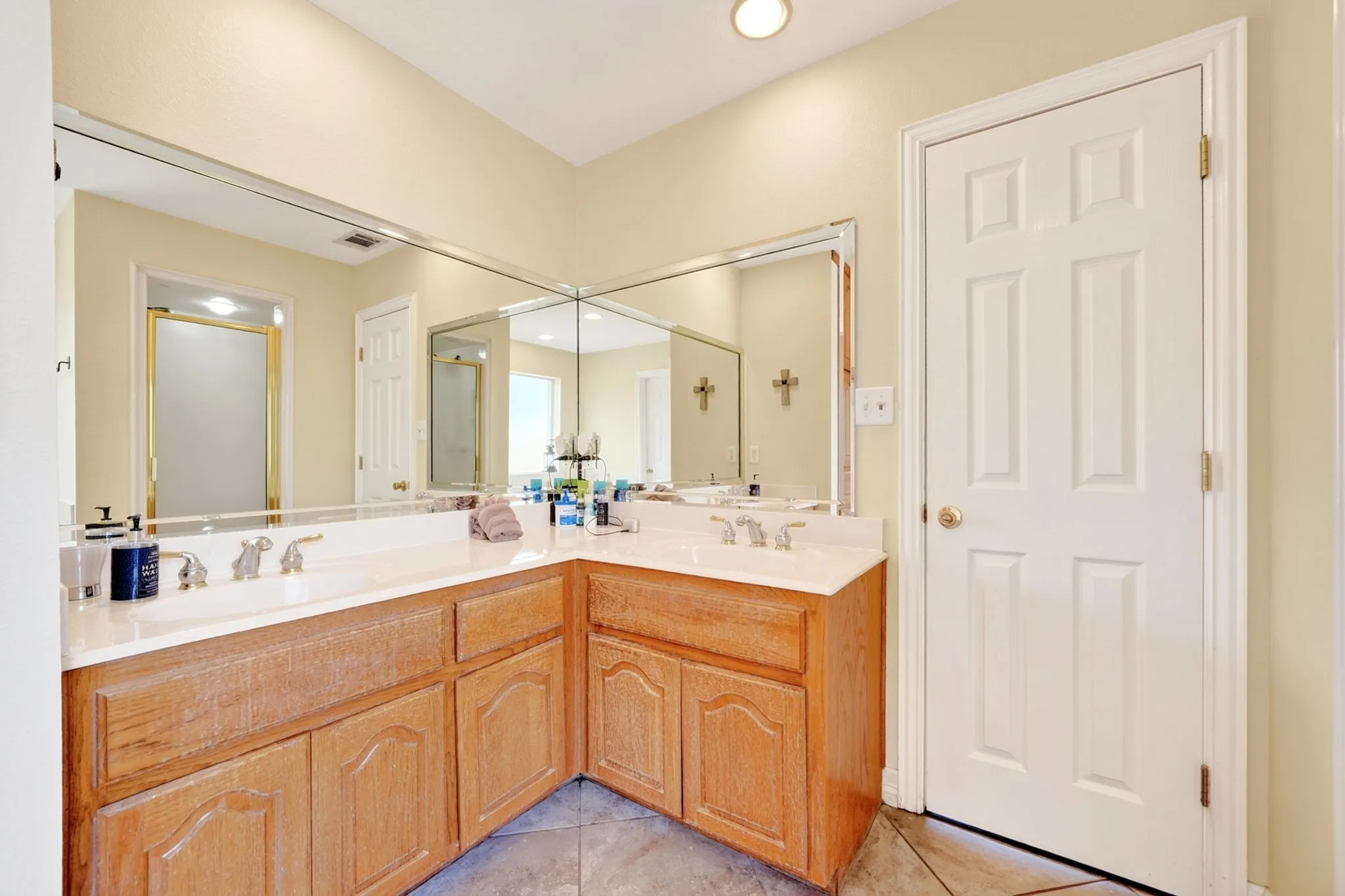 Dual undermount sinks with chrome fixtures, an expansive L-shaped vanity with wood-finish cabinetry, full-wall mirrors, and recessed ceiling lighting