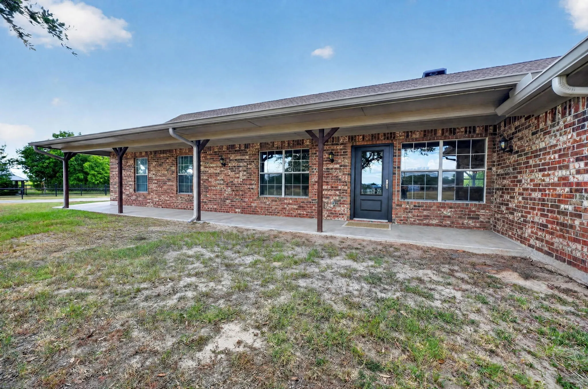 Brick exterior with an expansive covered patio, dark framed windows, and a black paneled entry door