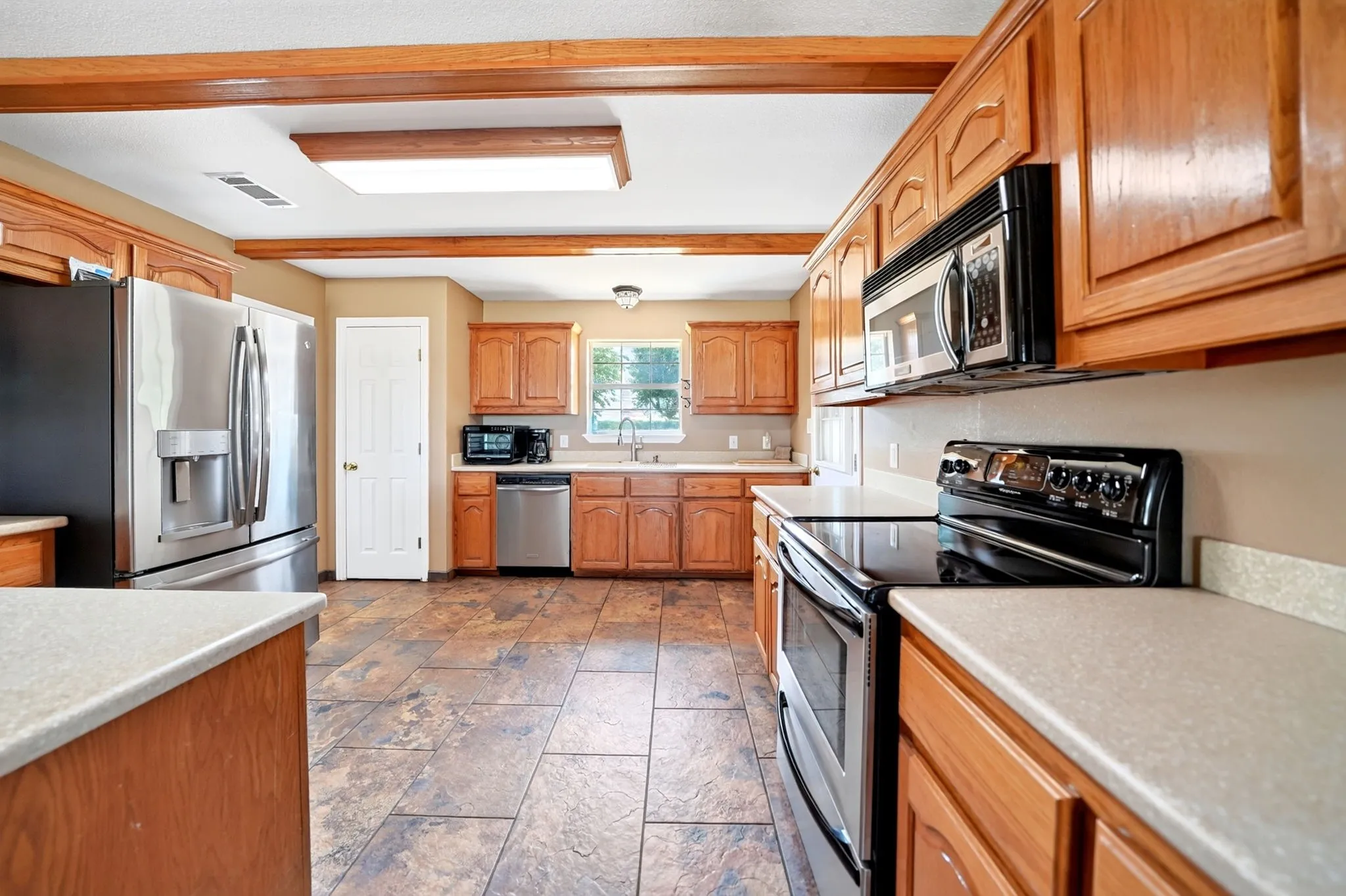 Kitchen featuring wood cabinetry, stainless steel appliances, durable tile flooring, and exposed ceiling beams