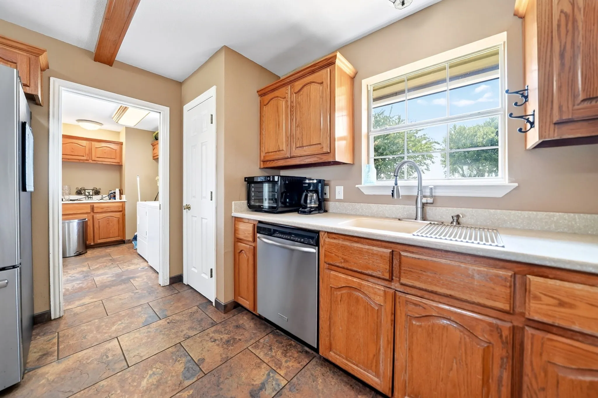 Wood cabinetry, stainless steel appliances, tile flooring, and a single basin sink with a gooseneck faucet
