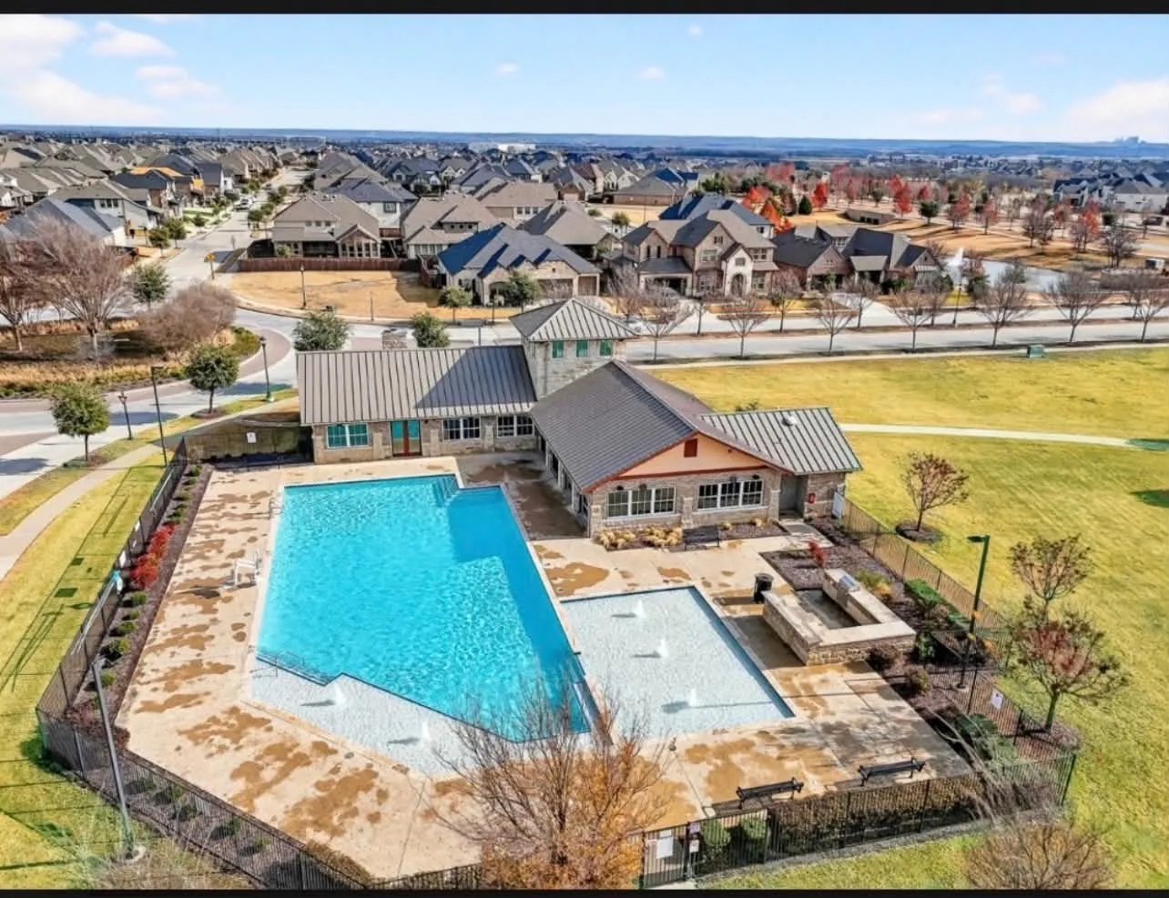Community amenity center featuring a stone-clad building with a metal roof, an outdoor swimming pool, a separate splash pad, and a stone-built hot tub