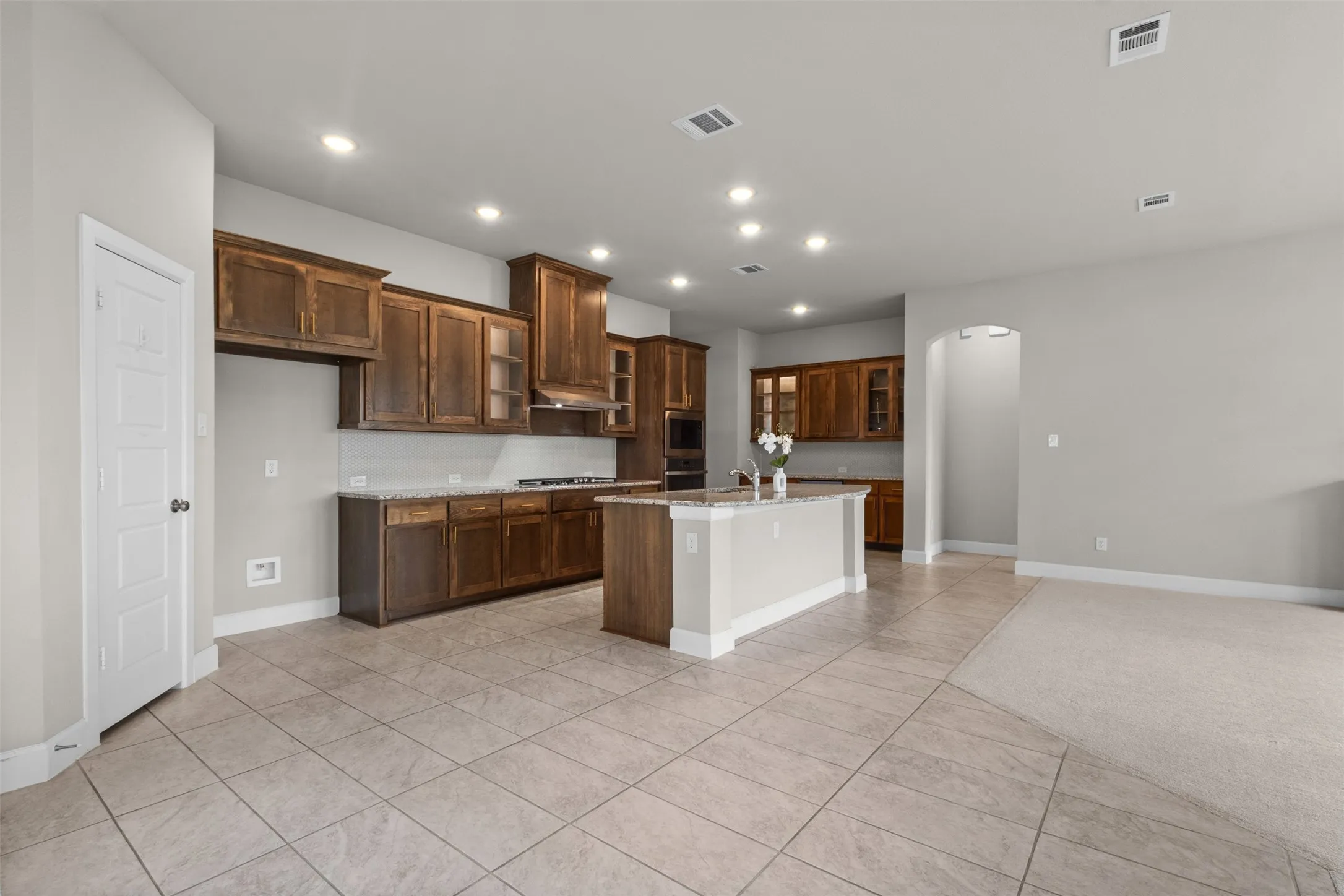 Open-concept kitchen featuring wood-finish cabinetry, a central island with a light-colored countertop, and recessed lighting