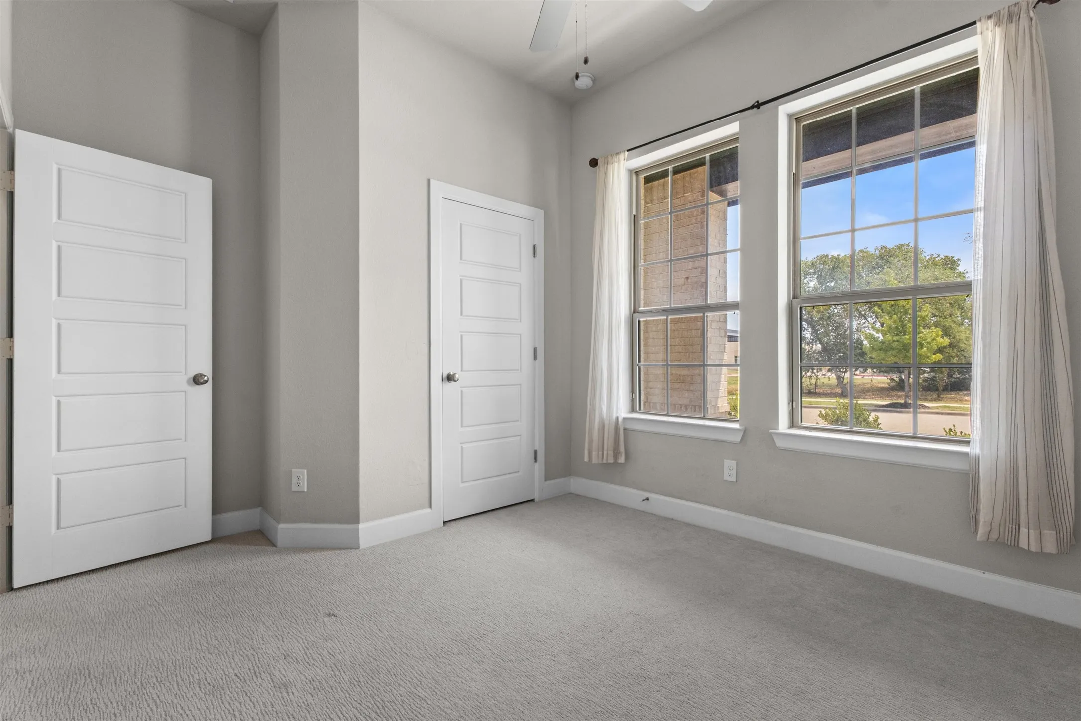 Neutral tone walls with white trim, two multi-pane windows, light gray carpet, and two paneled doors