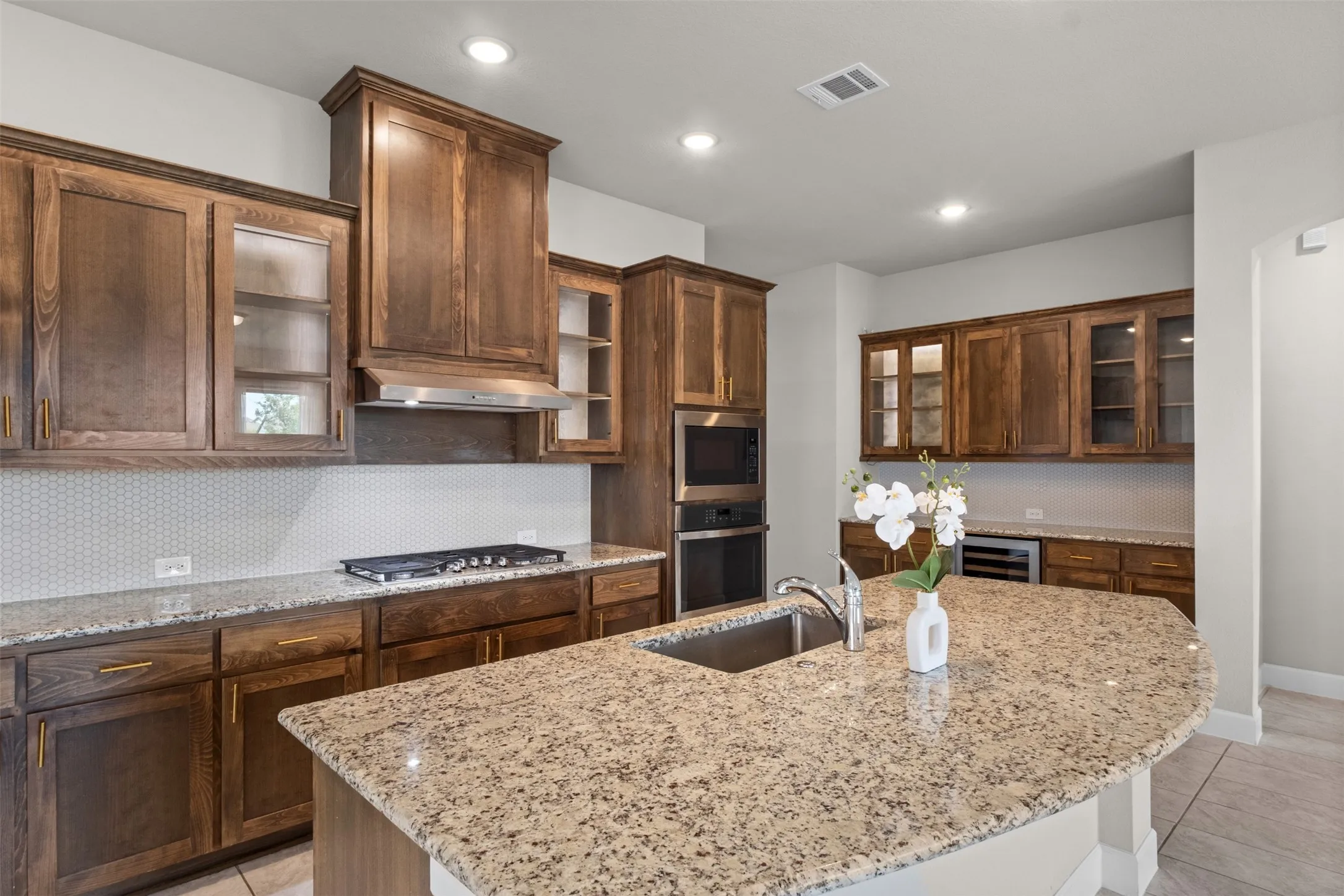 Kitchen featuring wood-finish cabinetry, a large island with sink, built-in double ovens, a gas cooktop, and a beverage cooler