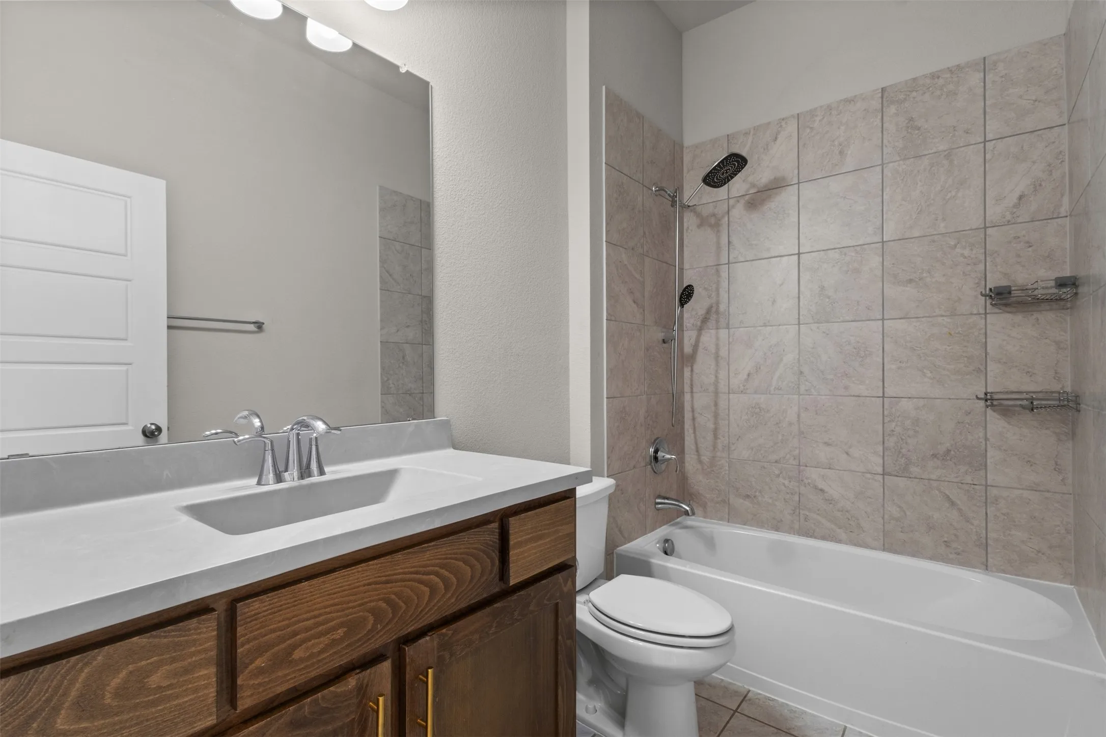 Bathroom featuring a wood-finish vanity, integrated sink, tiled tub surround, and a shower/tub combination