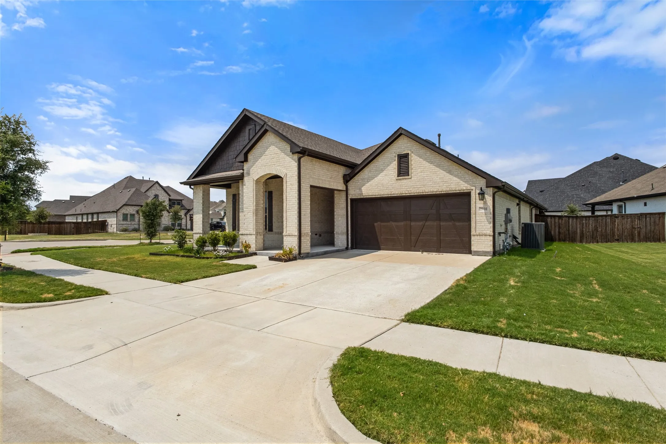Light-toned brick exterior with dark trim accents, an arched entry, a two-car garage, concrete driveway, and a manicured lawn