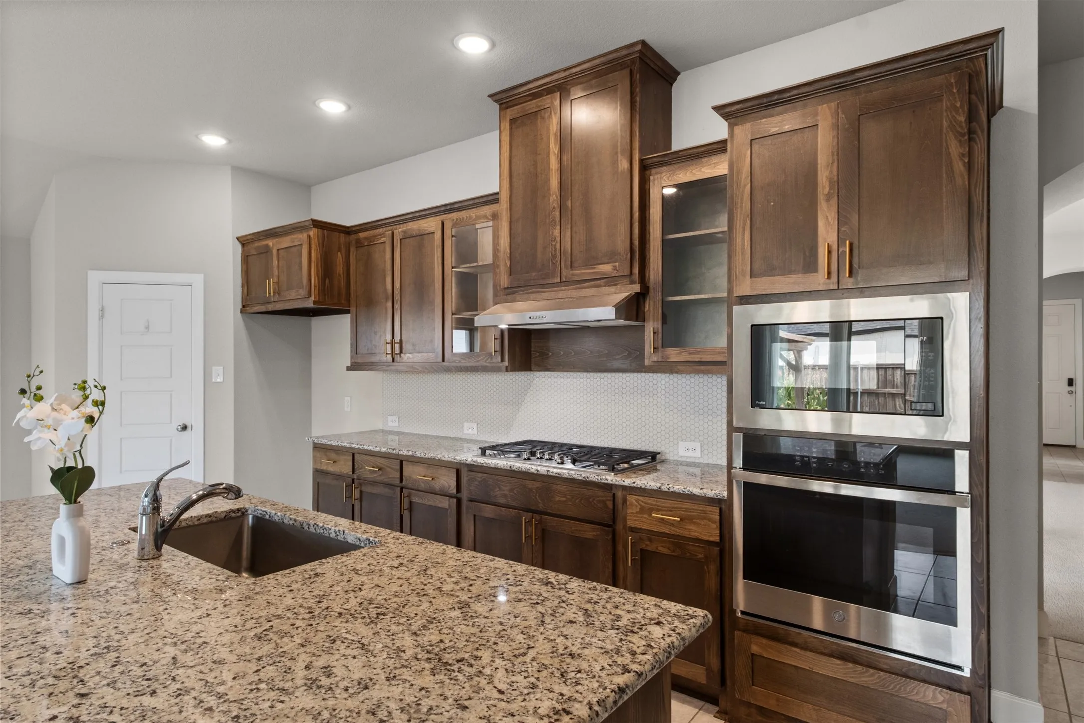 Kitchen featuring wood cabinetry, granite countertops, stainless steel appliances, a gas cooktop, and an integrated sink with a gooseneck faucet