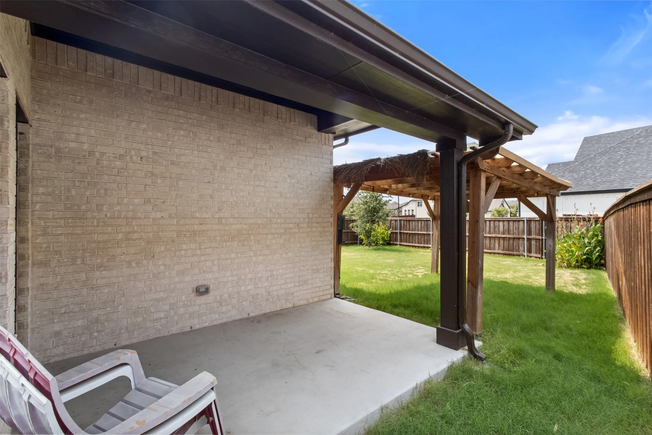 Covered concrete patio with a brick exterior, wood pergola, and fenced yard