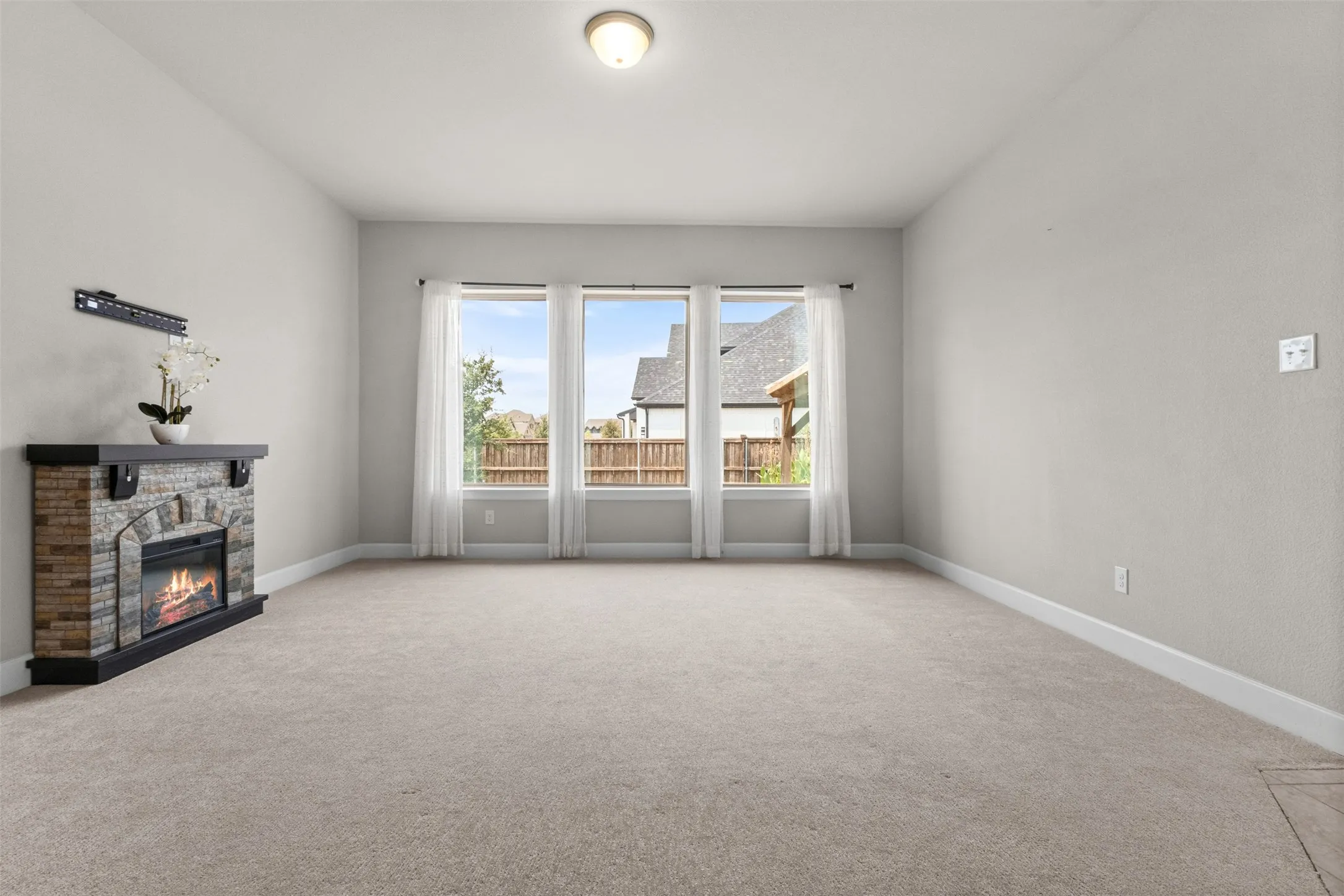 Spacious living room featuring triple glass doors opening to a covered deck, neutral carpet flooring, recessed ceiling lighting, and a brick fireplace with integrated mantel and hearth on the left wall
