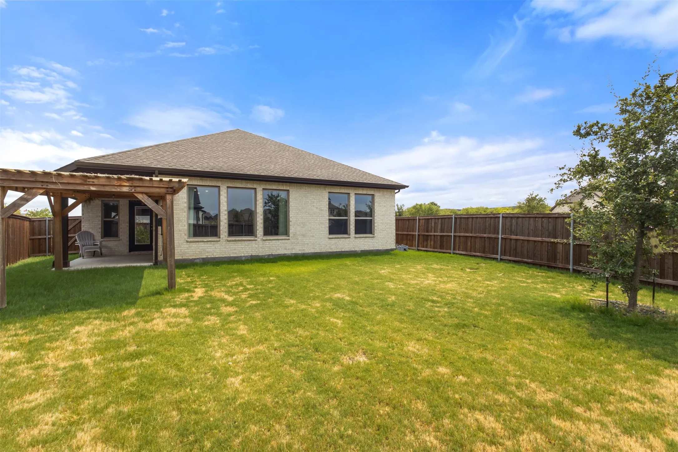 Expansive green lawn, wood pergola over a concrete patio, and a privacy fence