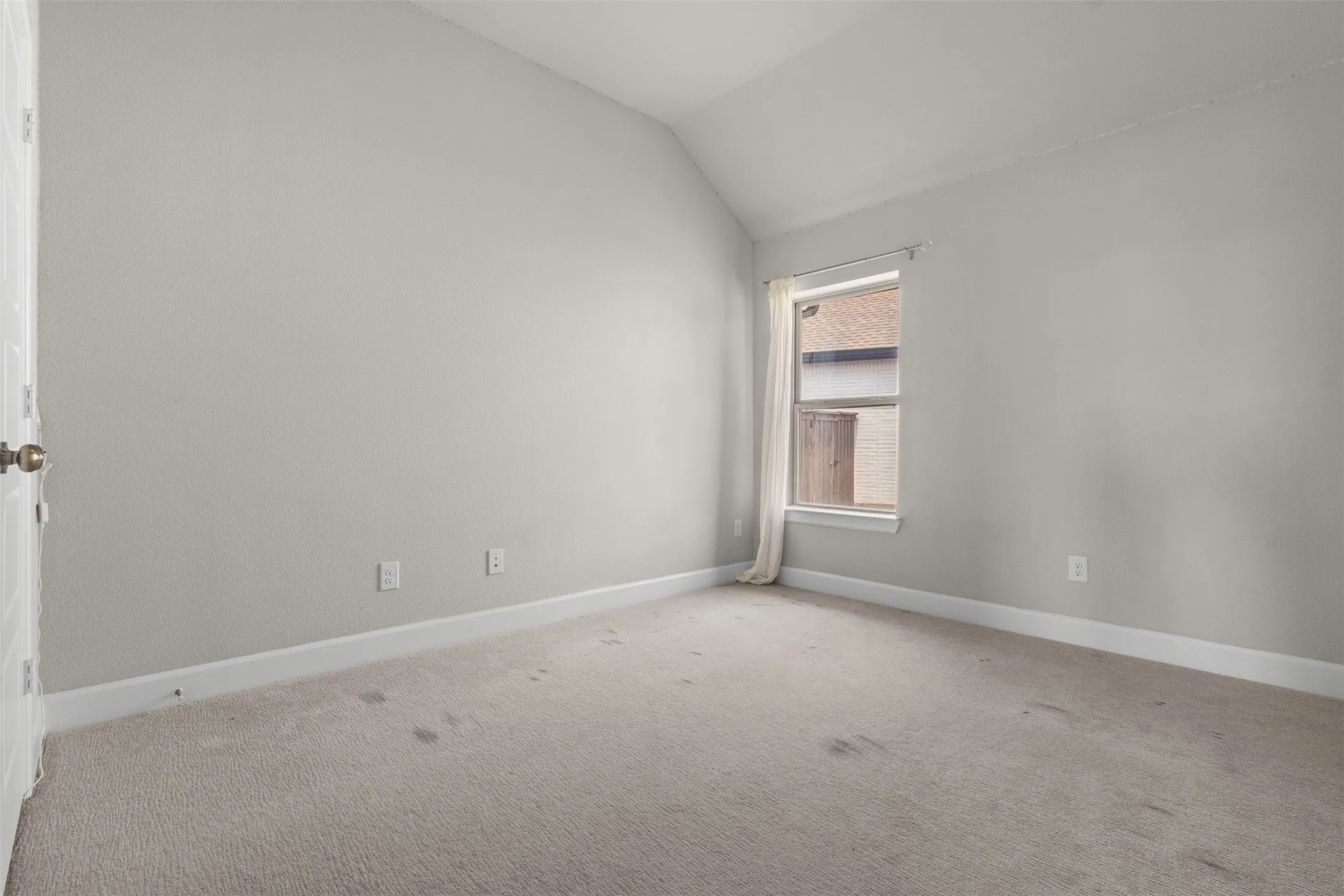 Vaulted ceiling room with neutral carpeting and a single window
