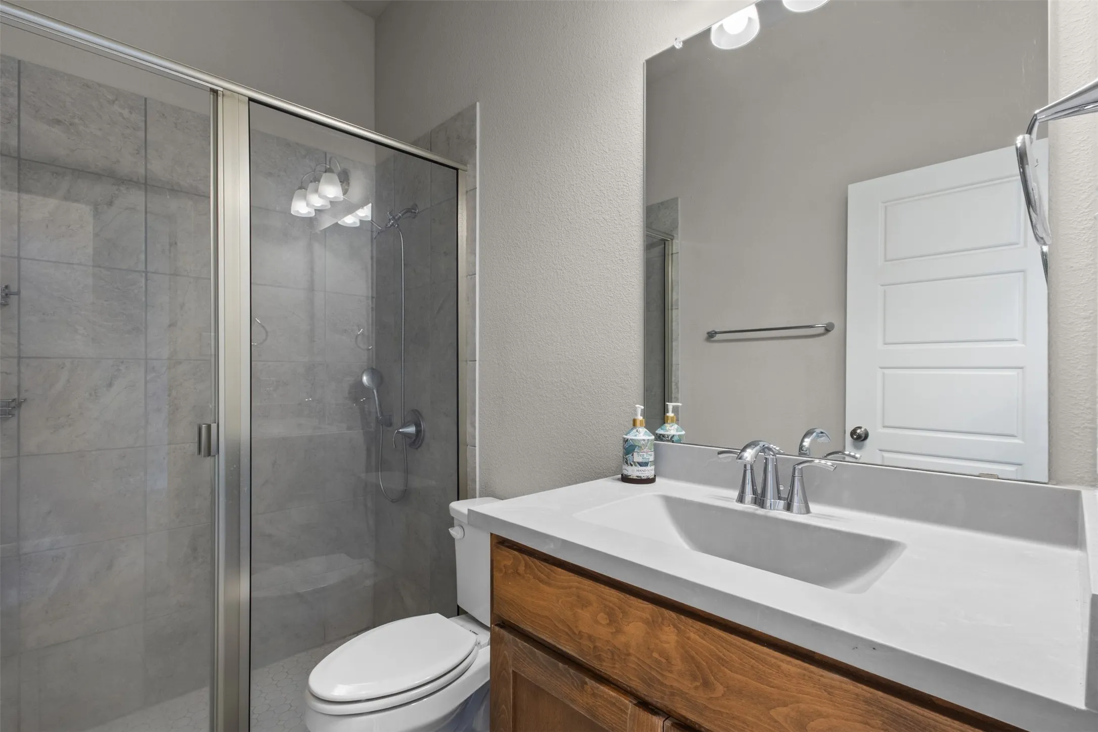 Glass-enclosed shower with tile surround, wood-finish vanity with an integrated sink, polished chrome fixtures, and a large wall mirror